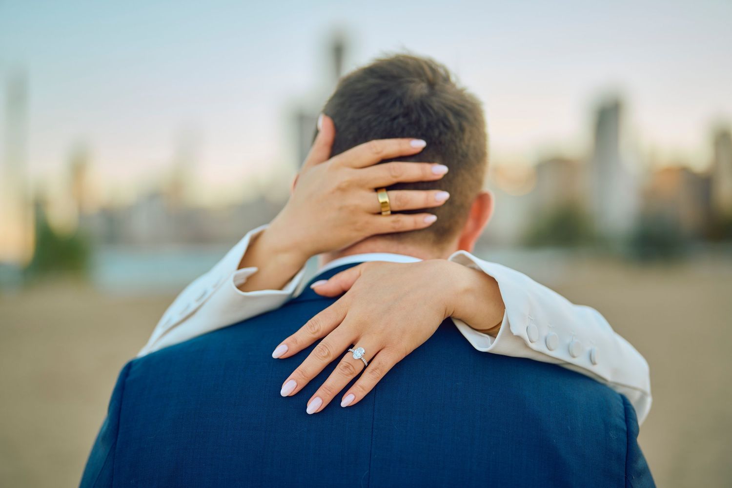 Back view of blue suited torso with hands embracing in a loving hug outdoors at sunset.