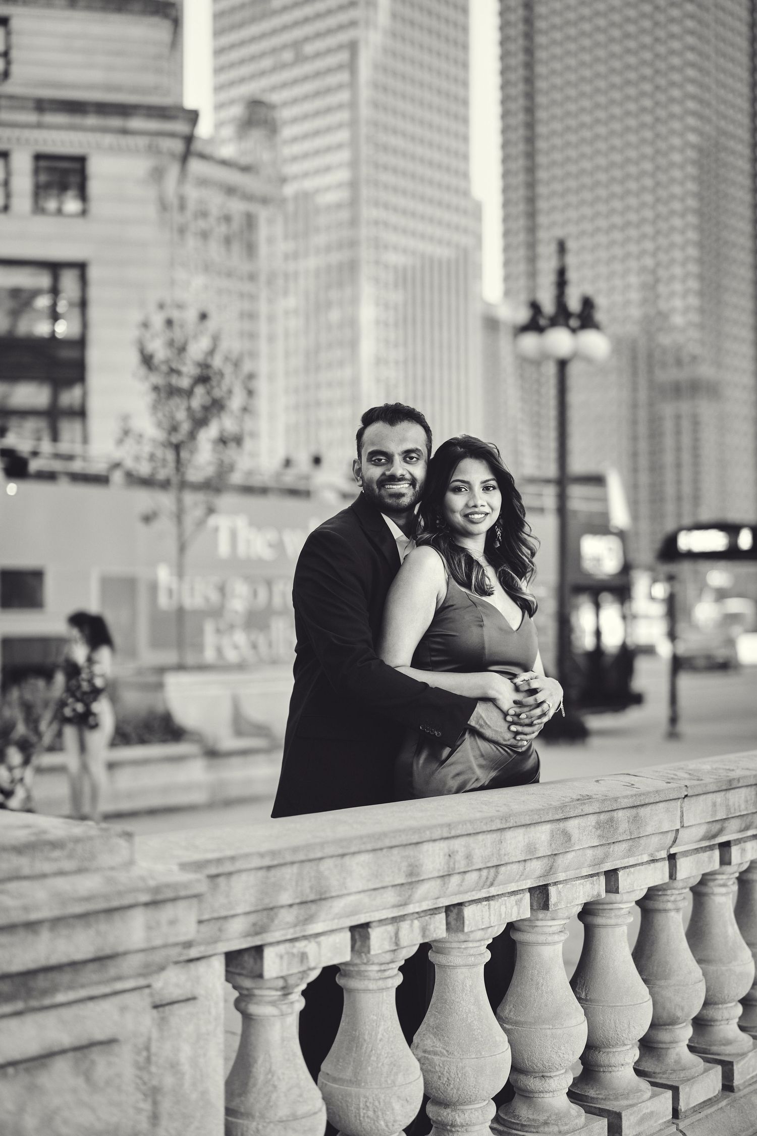 A romantic black and white portrait of a couple embracing on an urban balcony with city buildings in the background.