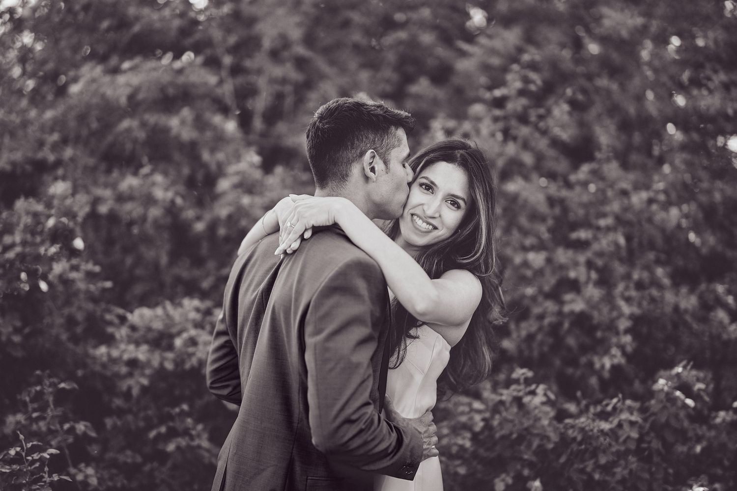 A romantic couple embraces while sharing an intimate moment in a garden setting.