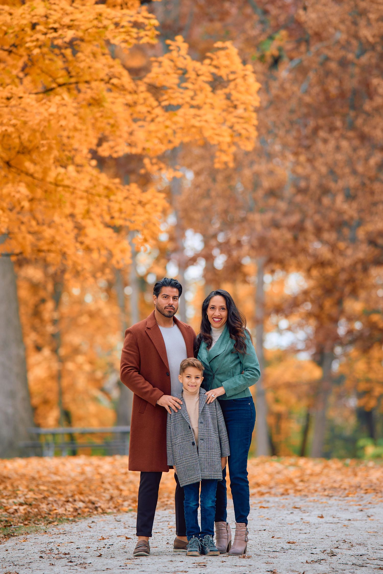 A family stands together on a path under vibrant golden autumn trees in a park.