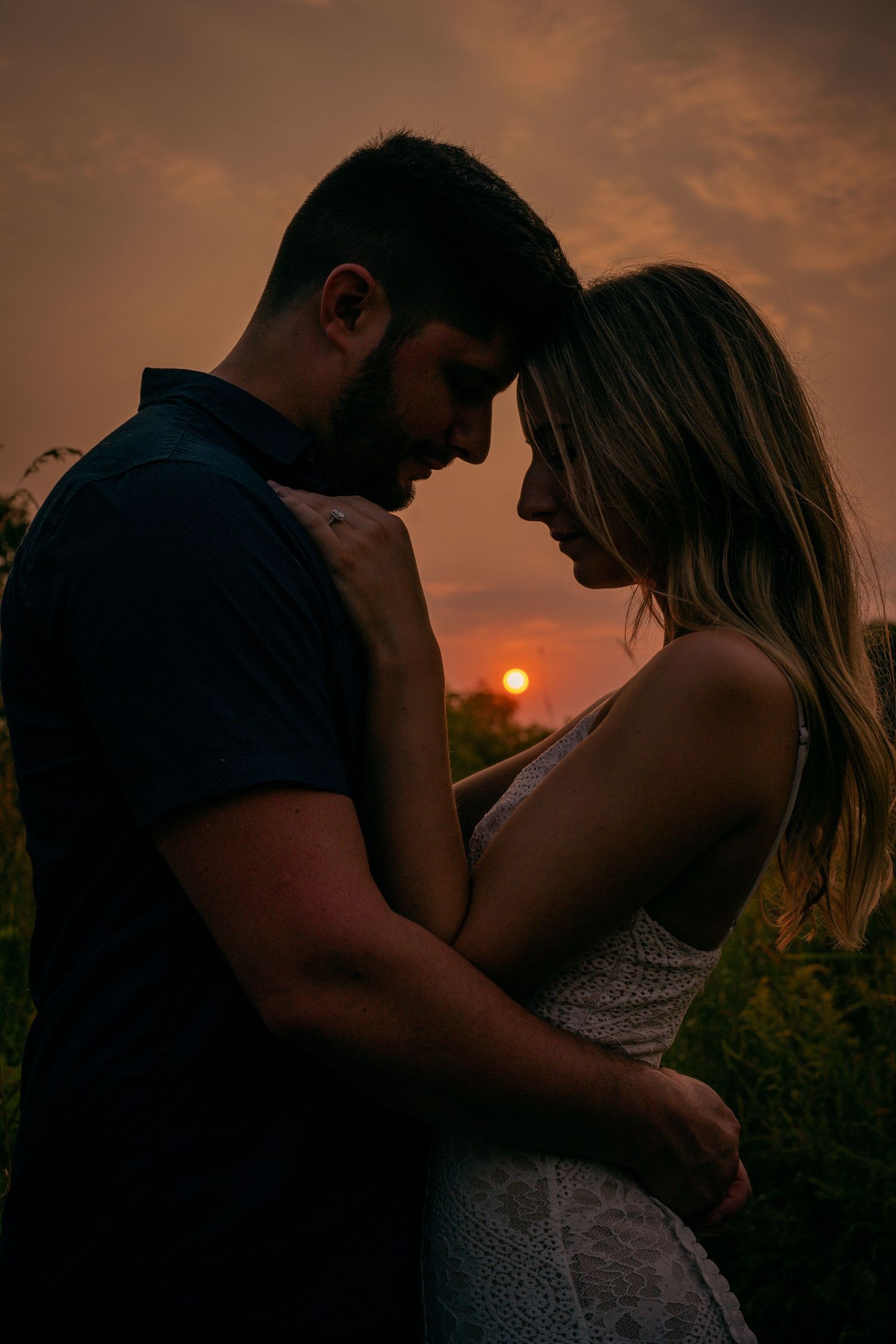 Silhouette of a romantic couple embracing at sunset with orange sky and glowing sun in background.