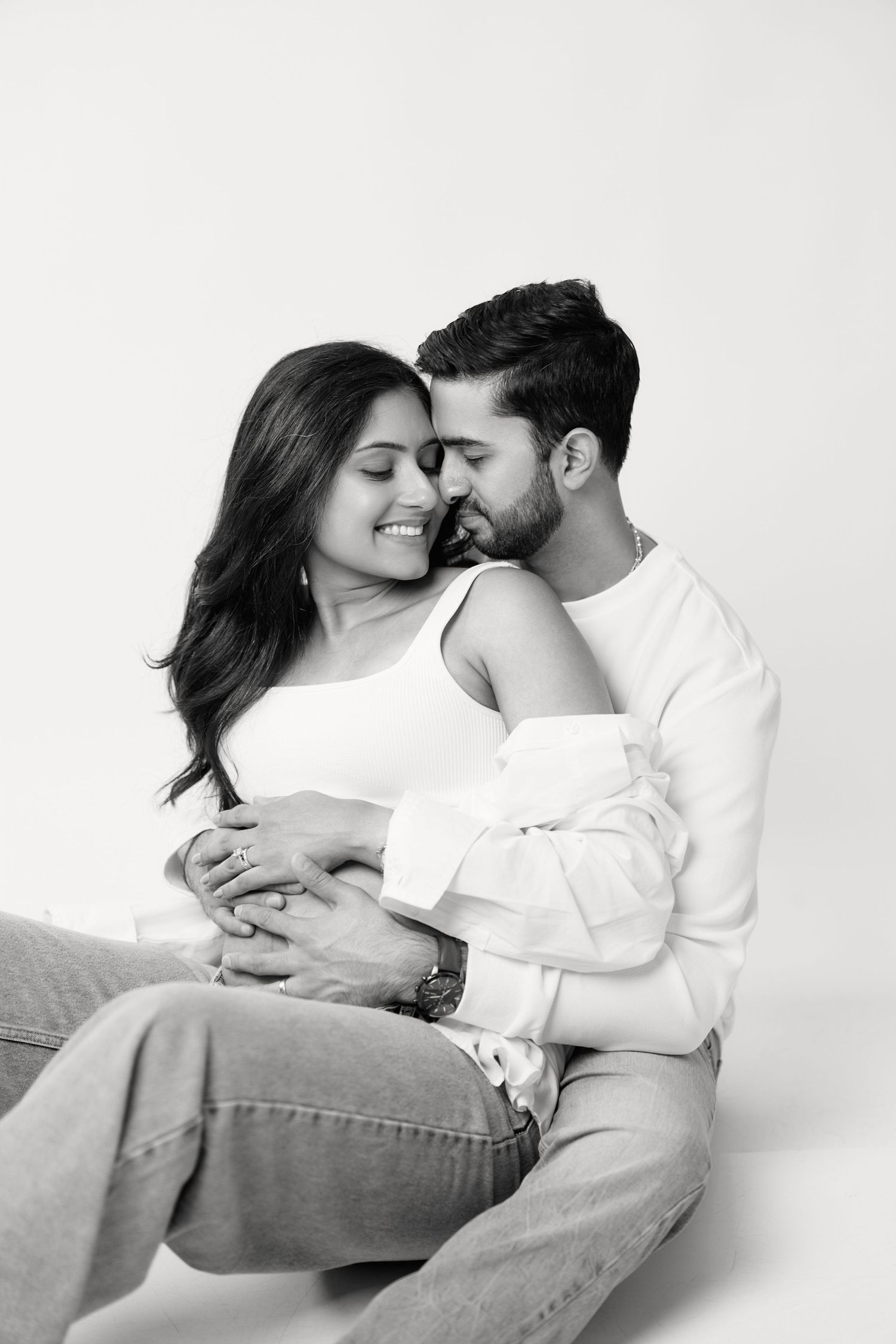 A couple shares an intimate moment in black and white as they embrace on a white background.