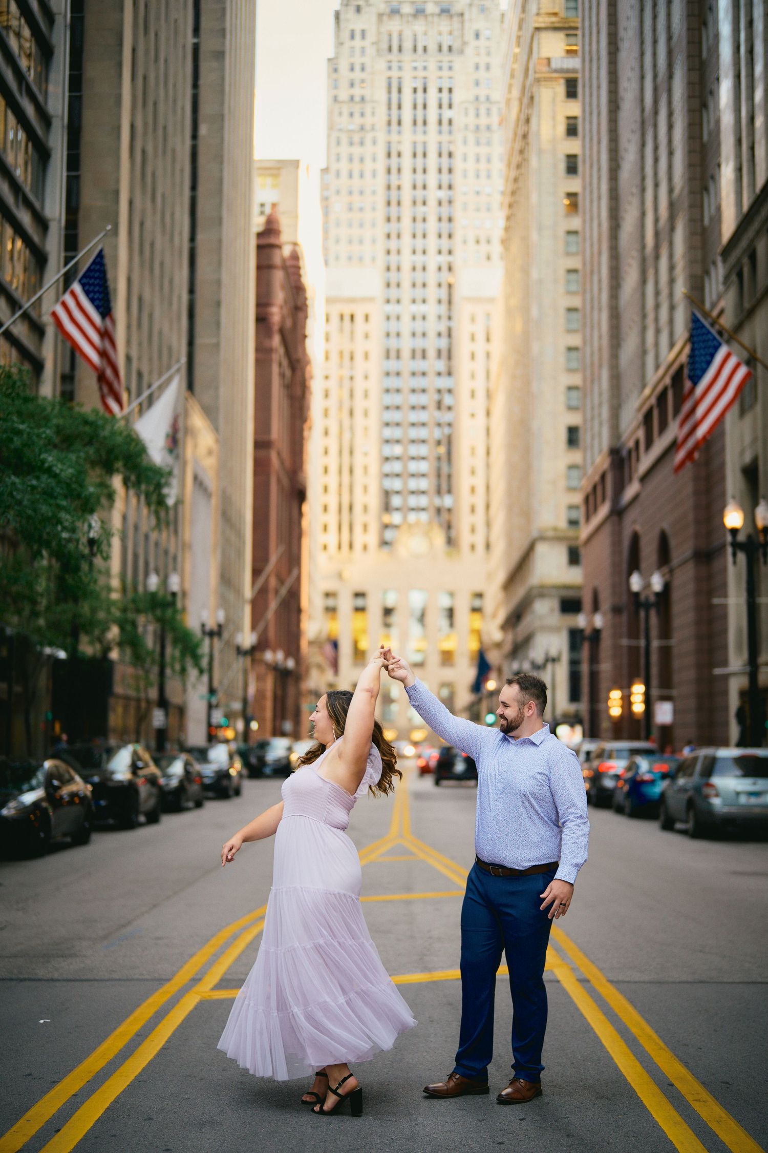 A couple dances in the middle of a city street lined with tall buildings and American flags in downtown Chicago.
