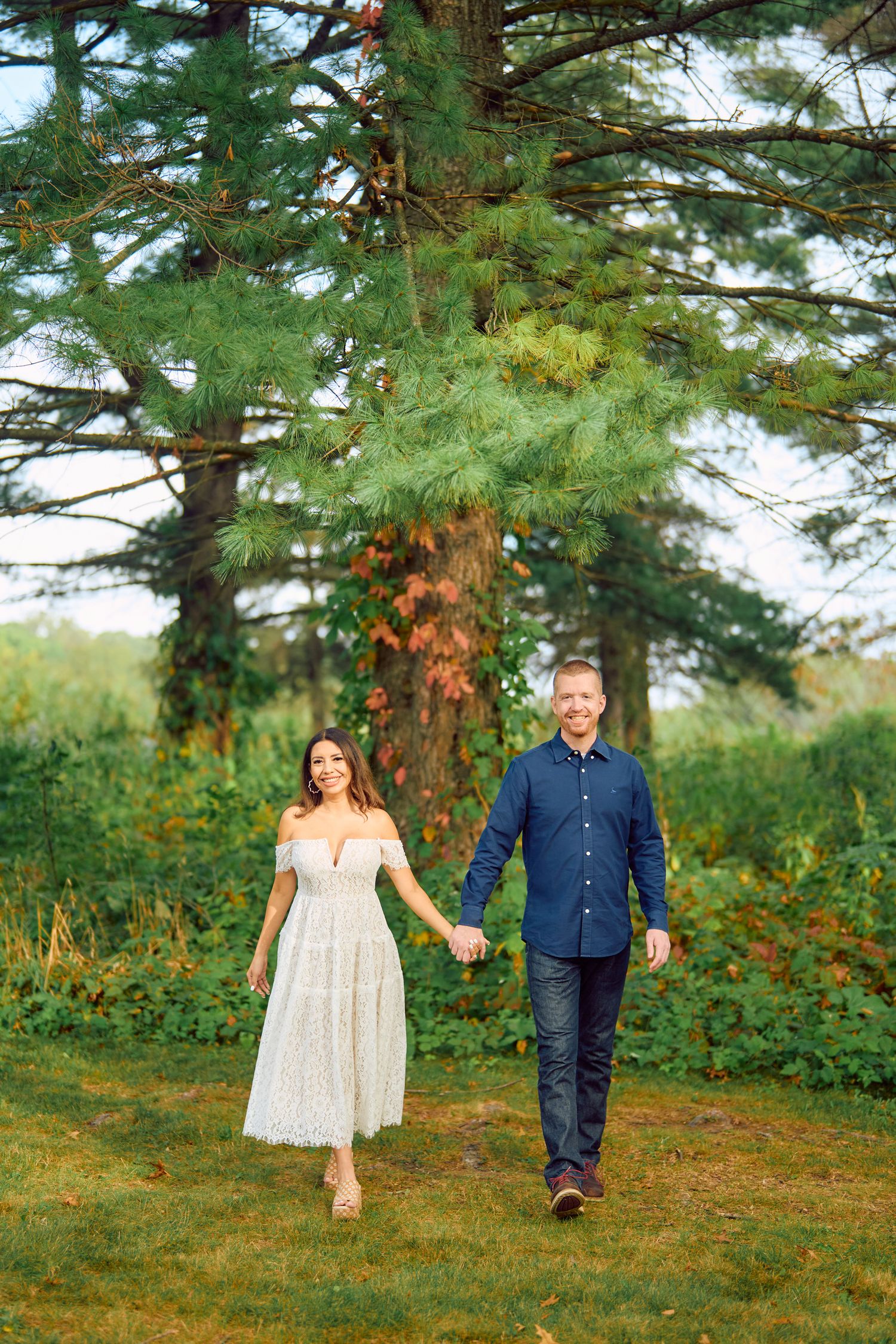 A couple takes a romantic walk together on a wooded path surrounded by tall pine trees in nature.