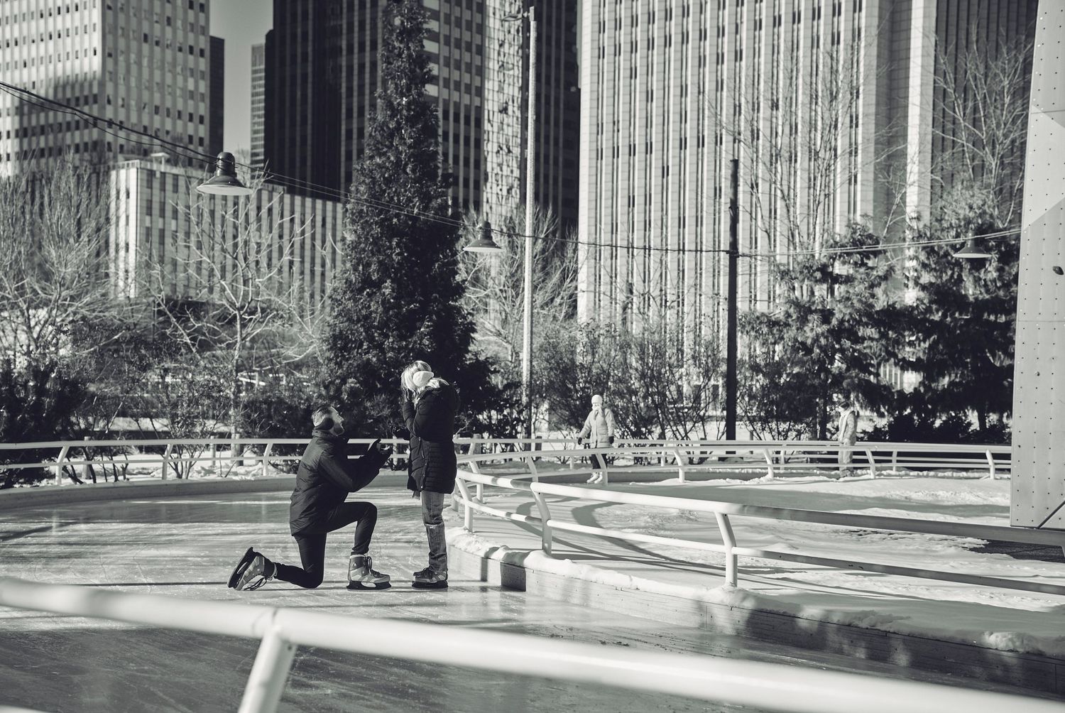 A marriage proposal moment captured in black and white at an urban park surrounded by skyscrapers.