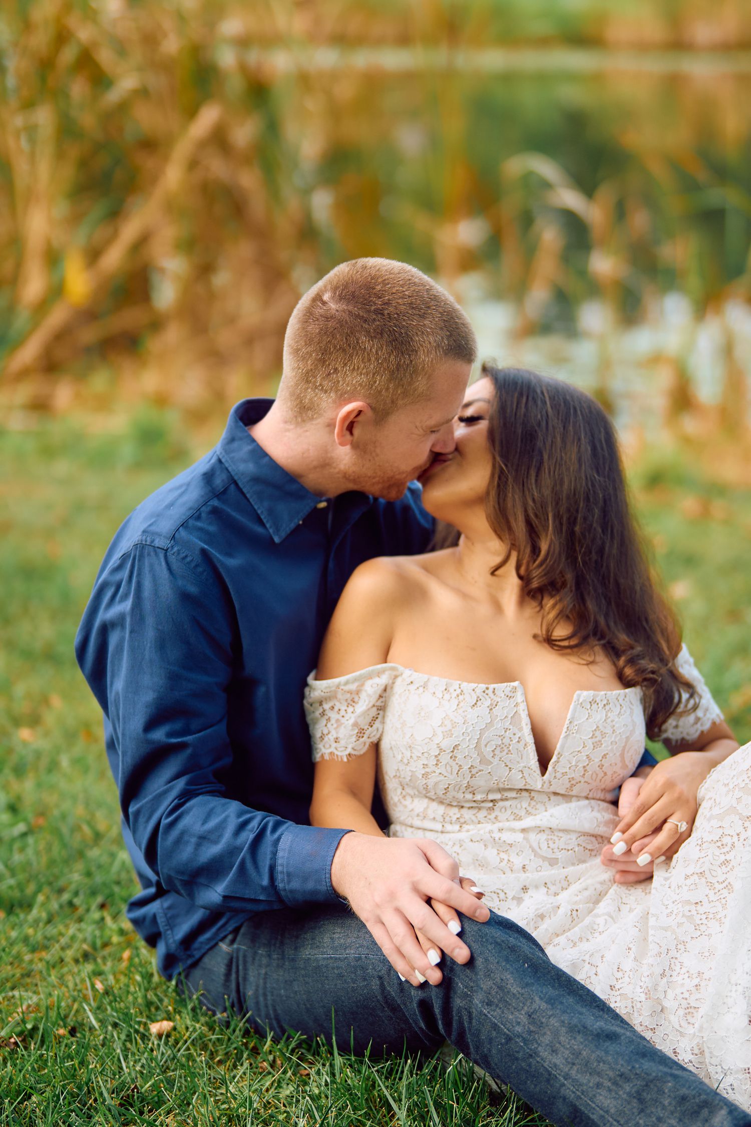A romantic outdoor portrait of a couple sitting in grass, sharing an intimate moment in golden natural lighting.