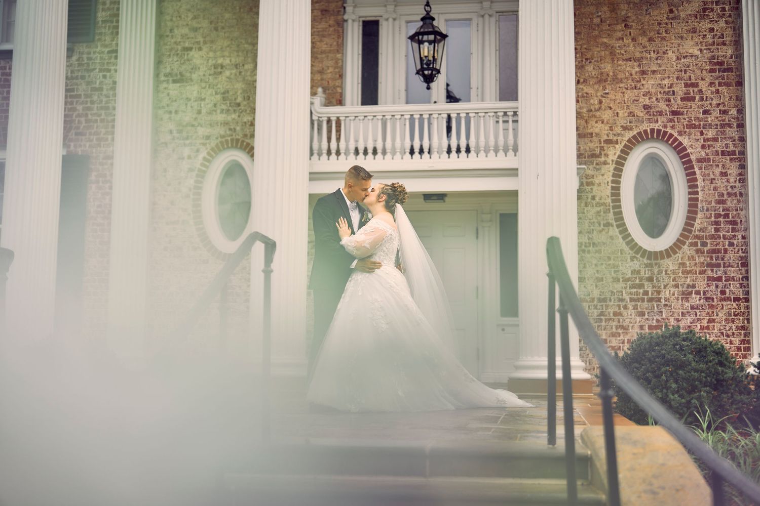 A romantic scene at a historic southern mansion with white balustrades and oval windows amid soft fog.