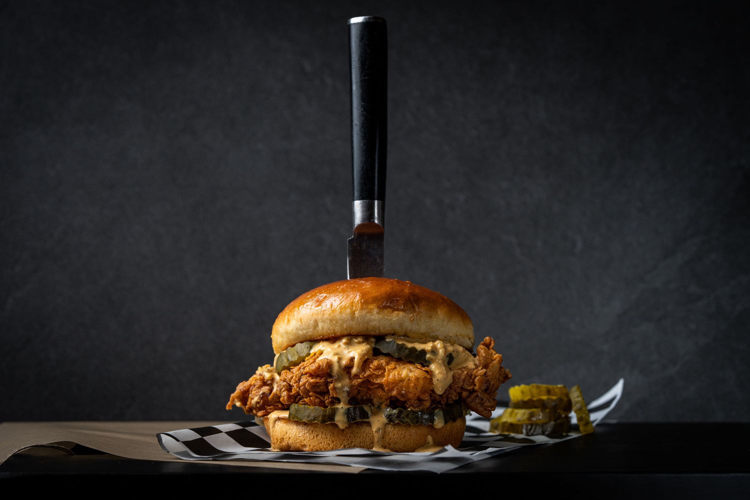 Gourmet burger with knife on dark background in dramatic lighting.
