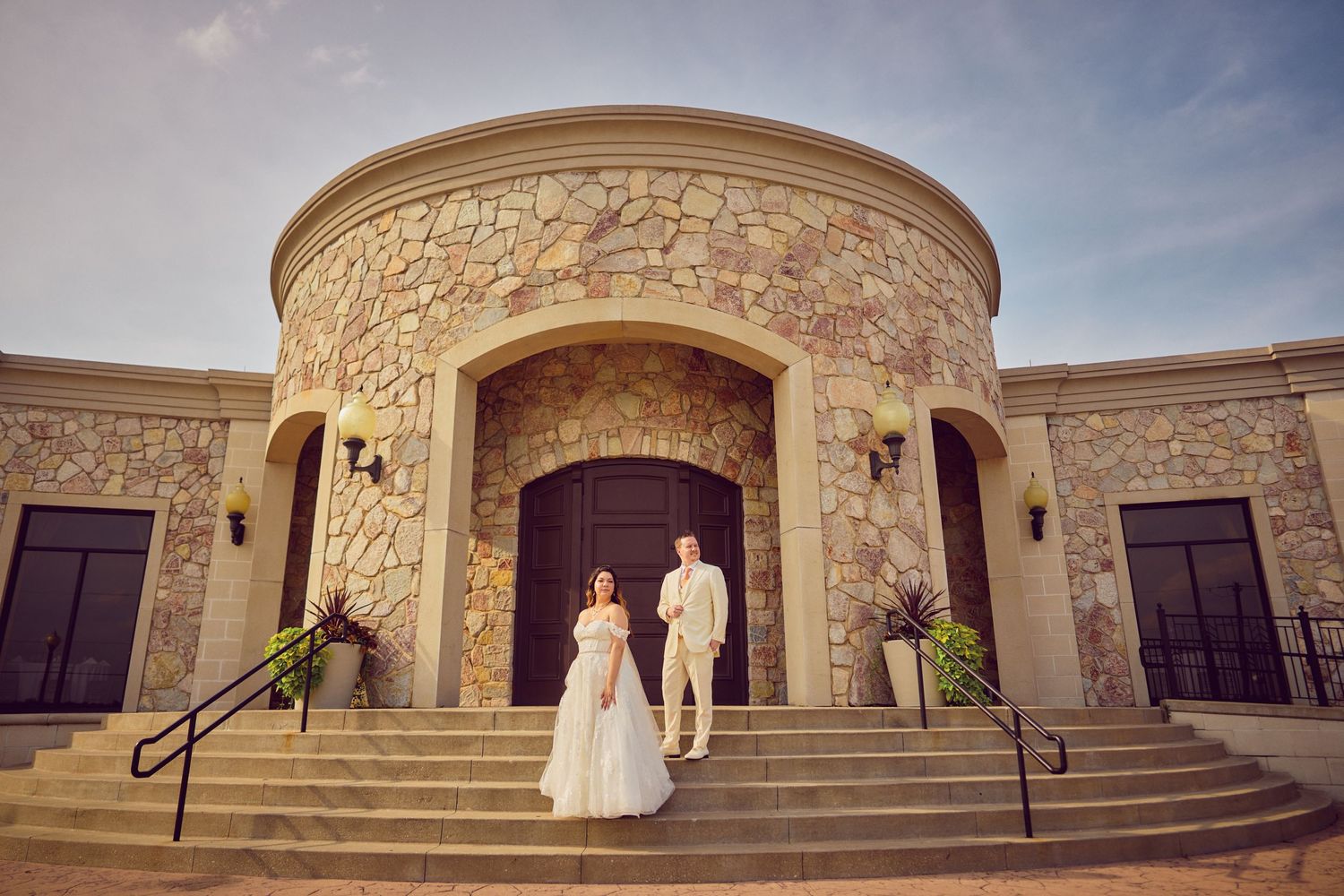 A stone building entrance with ornate carvings features grand stairs and dark wood doors under a cloudy sky.