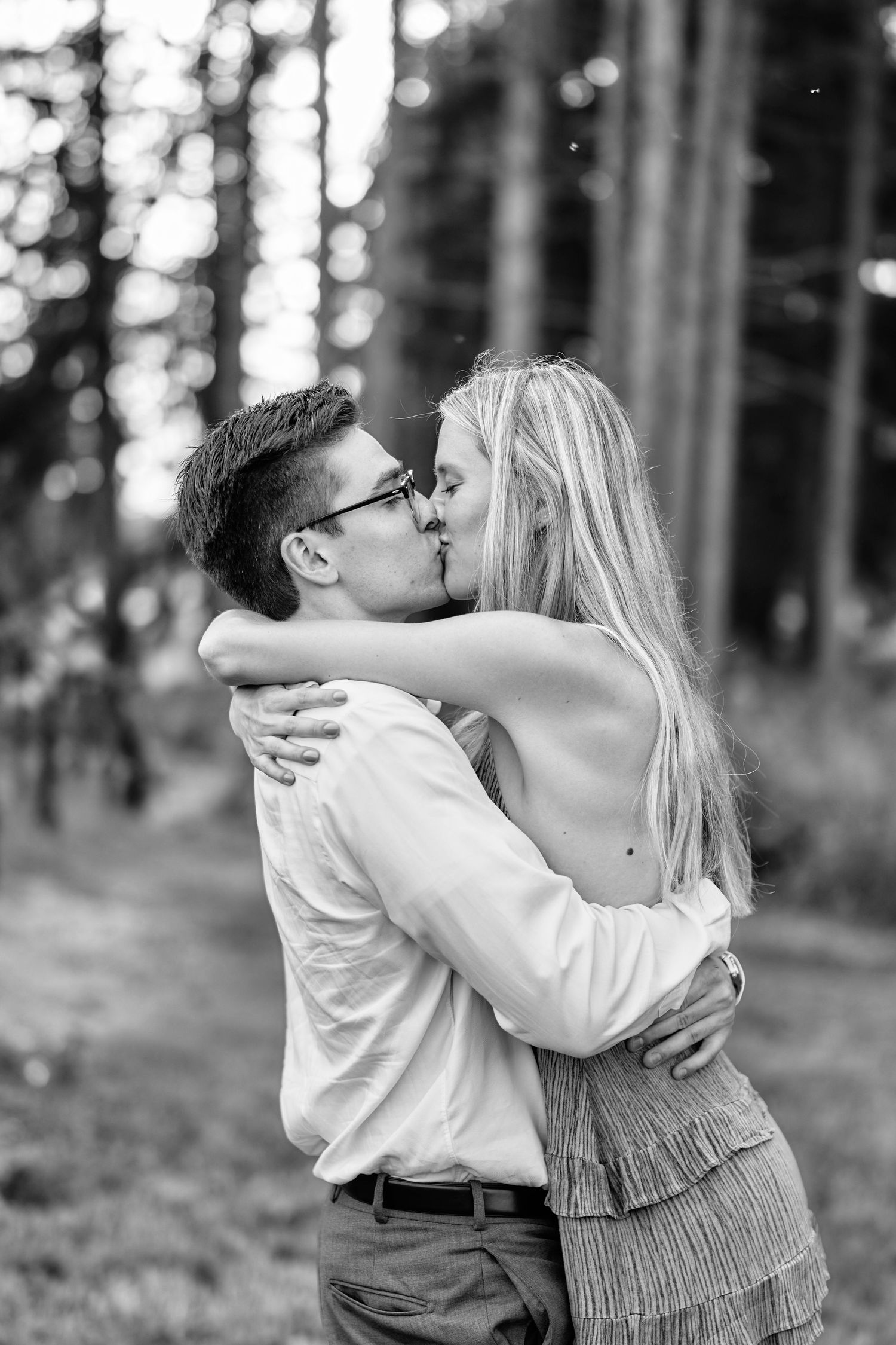 A romantic black and white photo of a couple sharing a tender kiss in a forest setting.