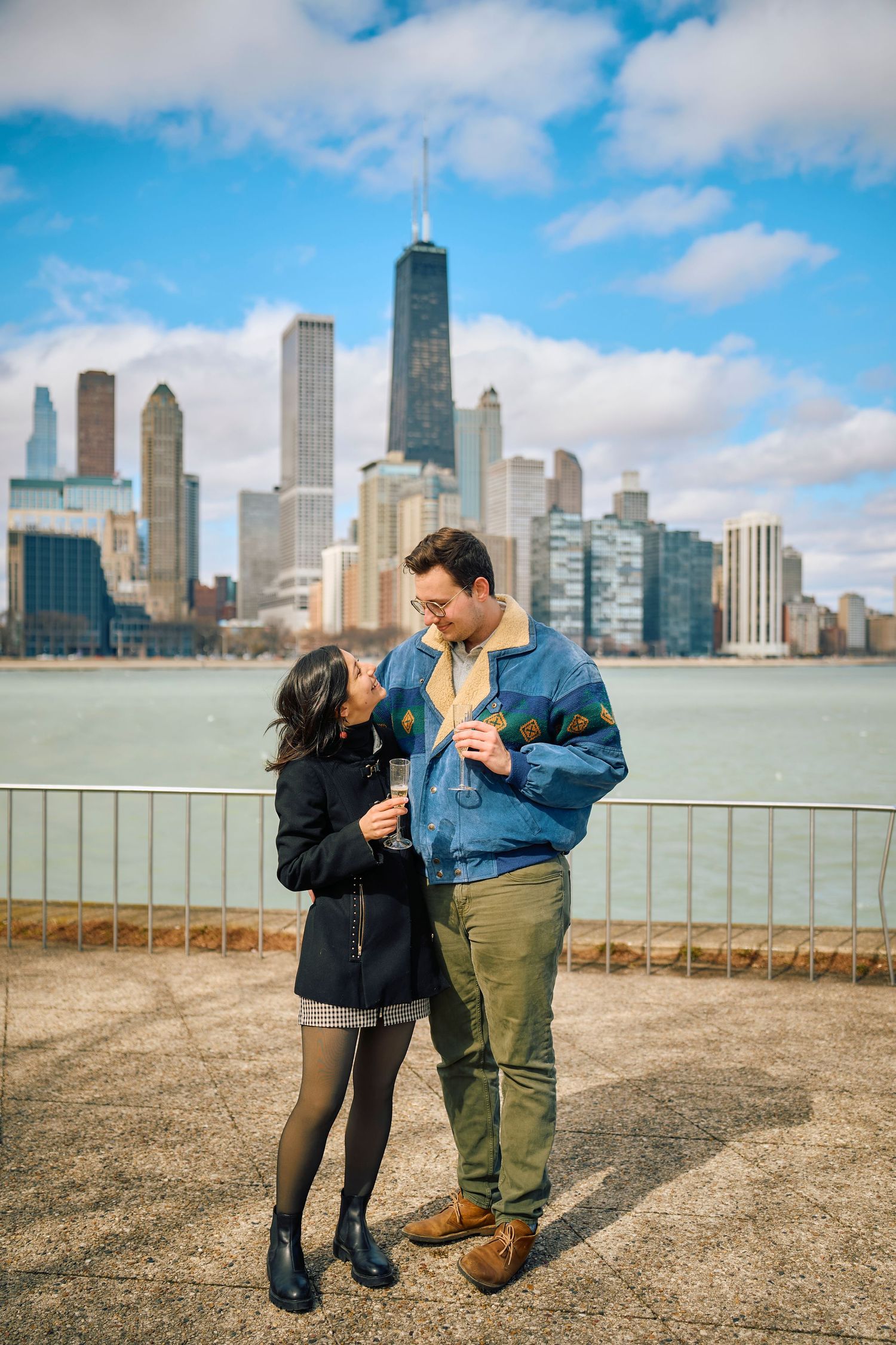 A couple shares a tender moment against the Chicago skyline backdrop on a sunny day by the waterfront.
