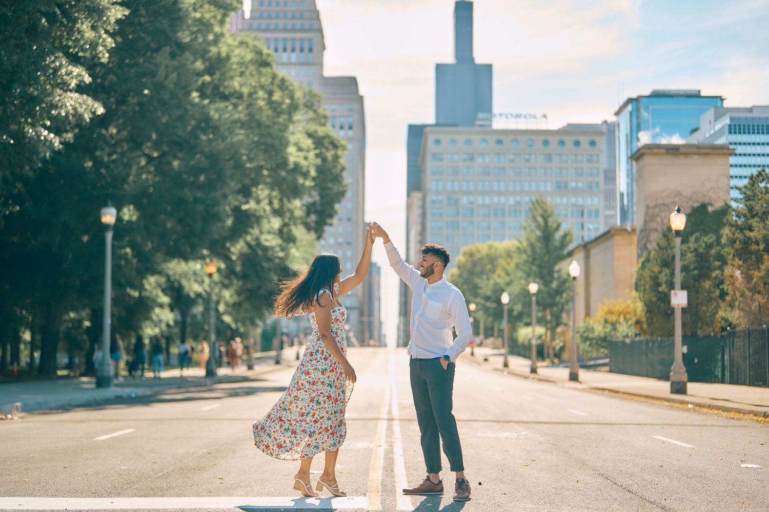 Two people dance together on an empty city street with tall buildings and trees in Chicago on a sunny day.