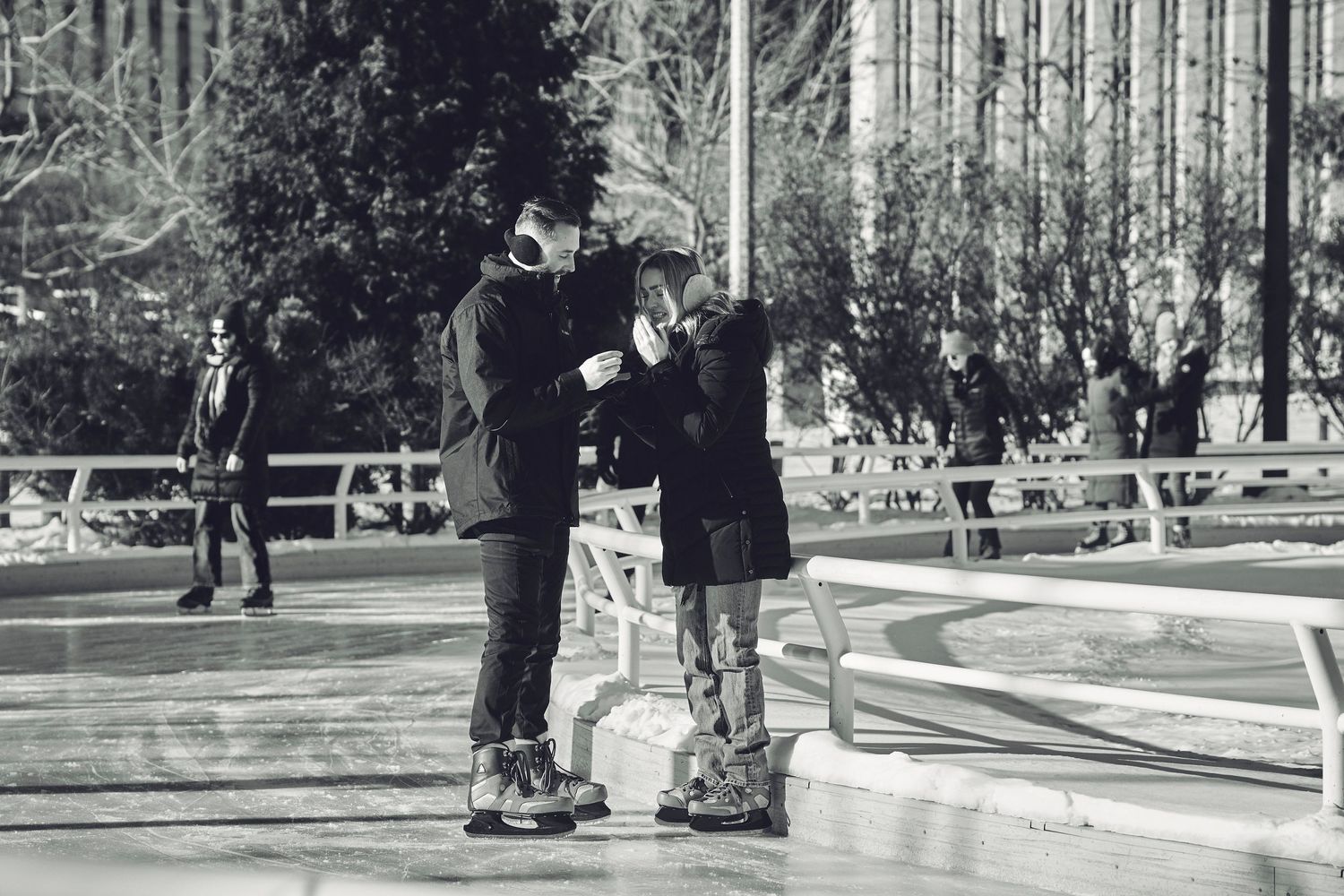 A couple stands together on rollerblades in a park setting, captured in black and white.