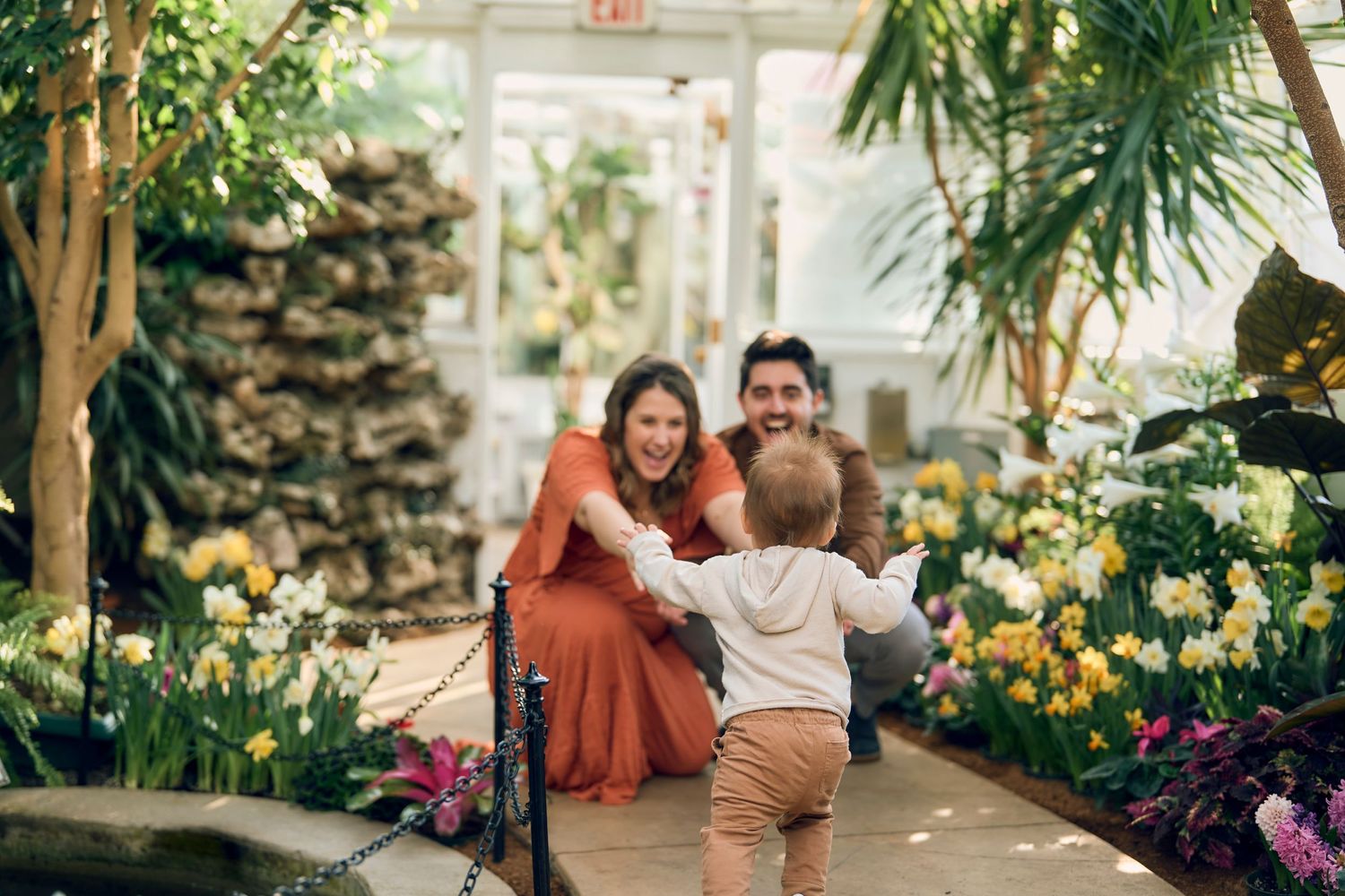 Family spending time together in a lush greenhouse surrounded by colorful flowers and tropical plants.