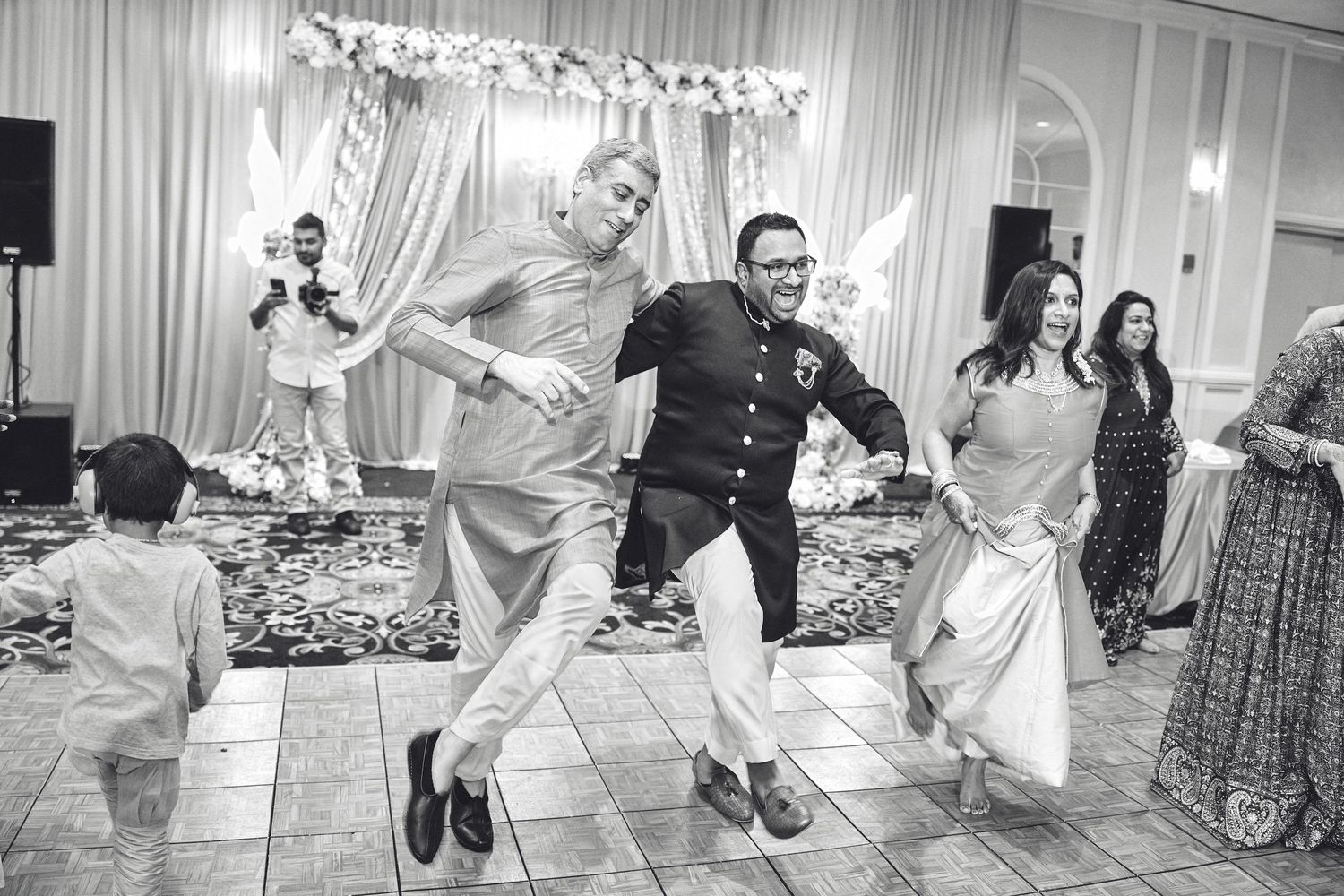 Joyful guests leap and dance together on the reception dance floor while celebrating at an elegant wedding.