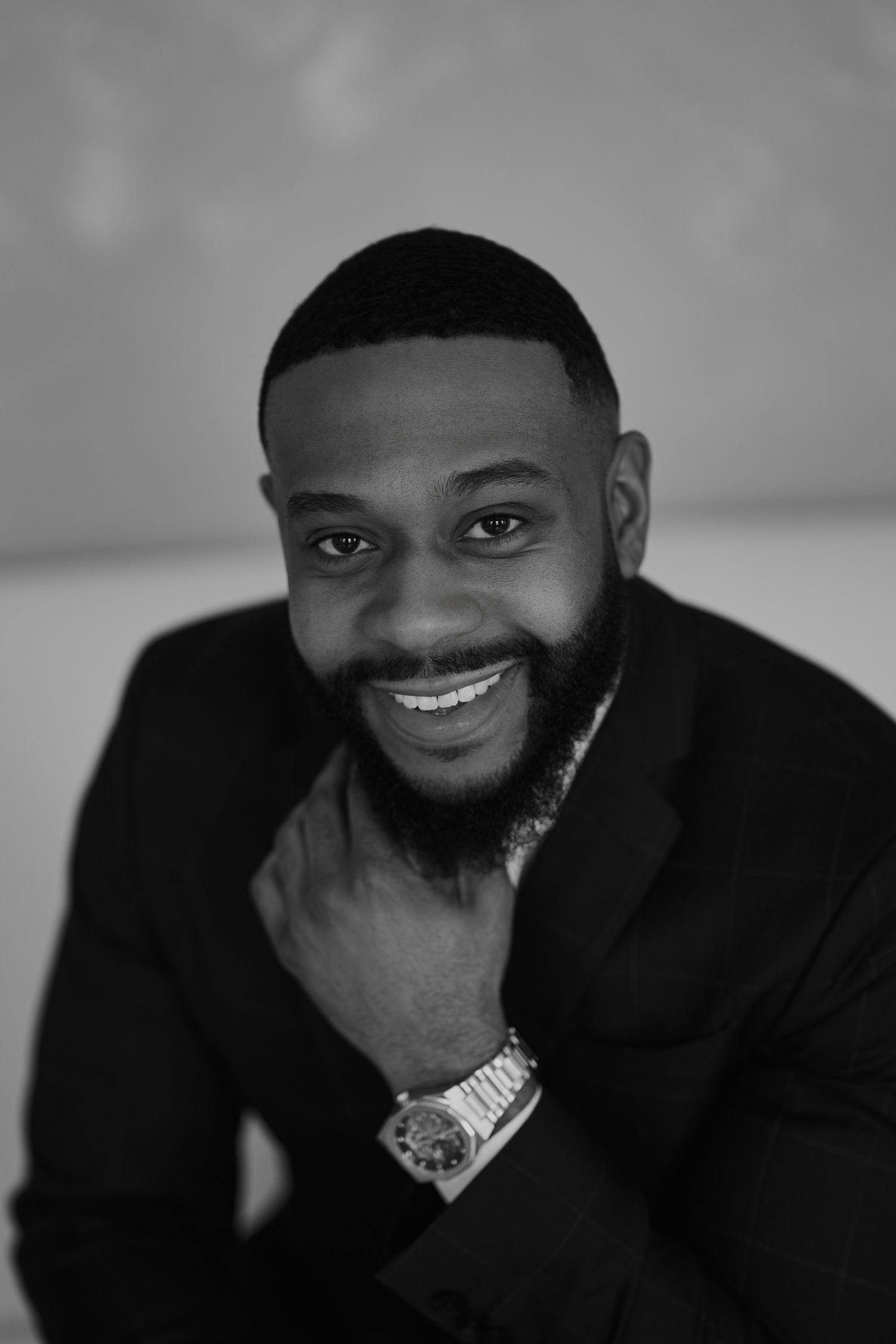 Black and white portrait of person in dark blazer wearing luxury watch and smiling.