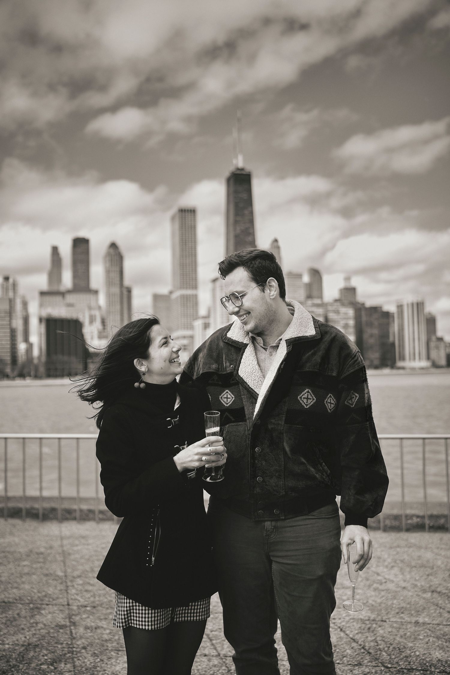 Black and white photo of couple sharing tender moment with Chicago skyline in background.