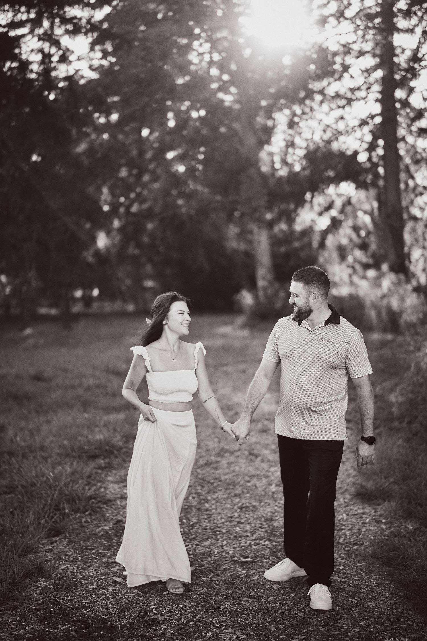 Romantic couple walking hand in hand through a sunlit forest path in black and white photography.