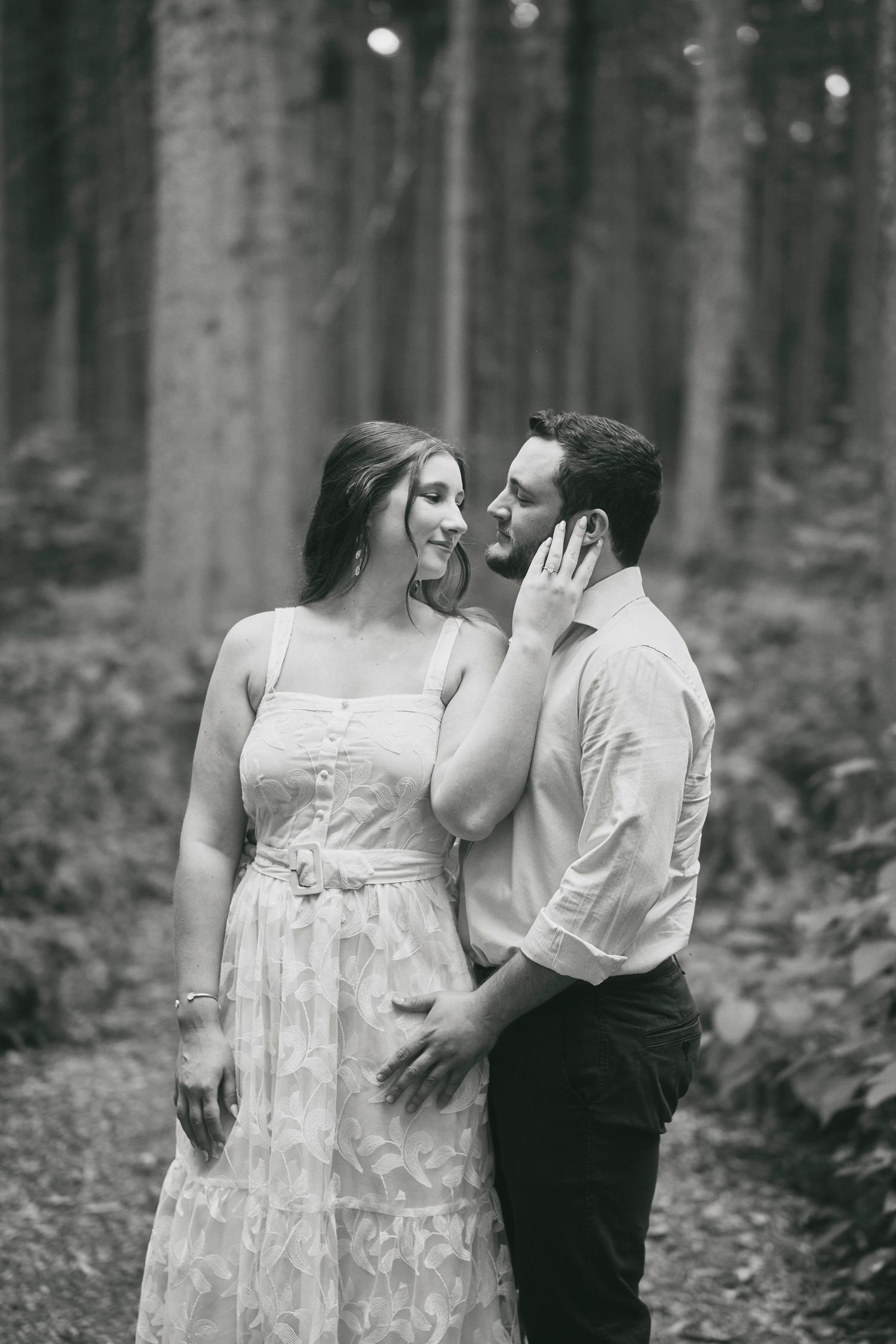 A romantic couple embraces in a misty forest setting, captured in black and white photography.