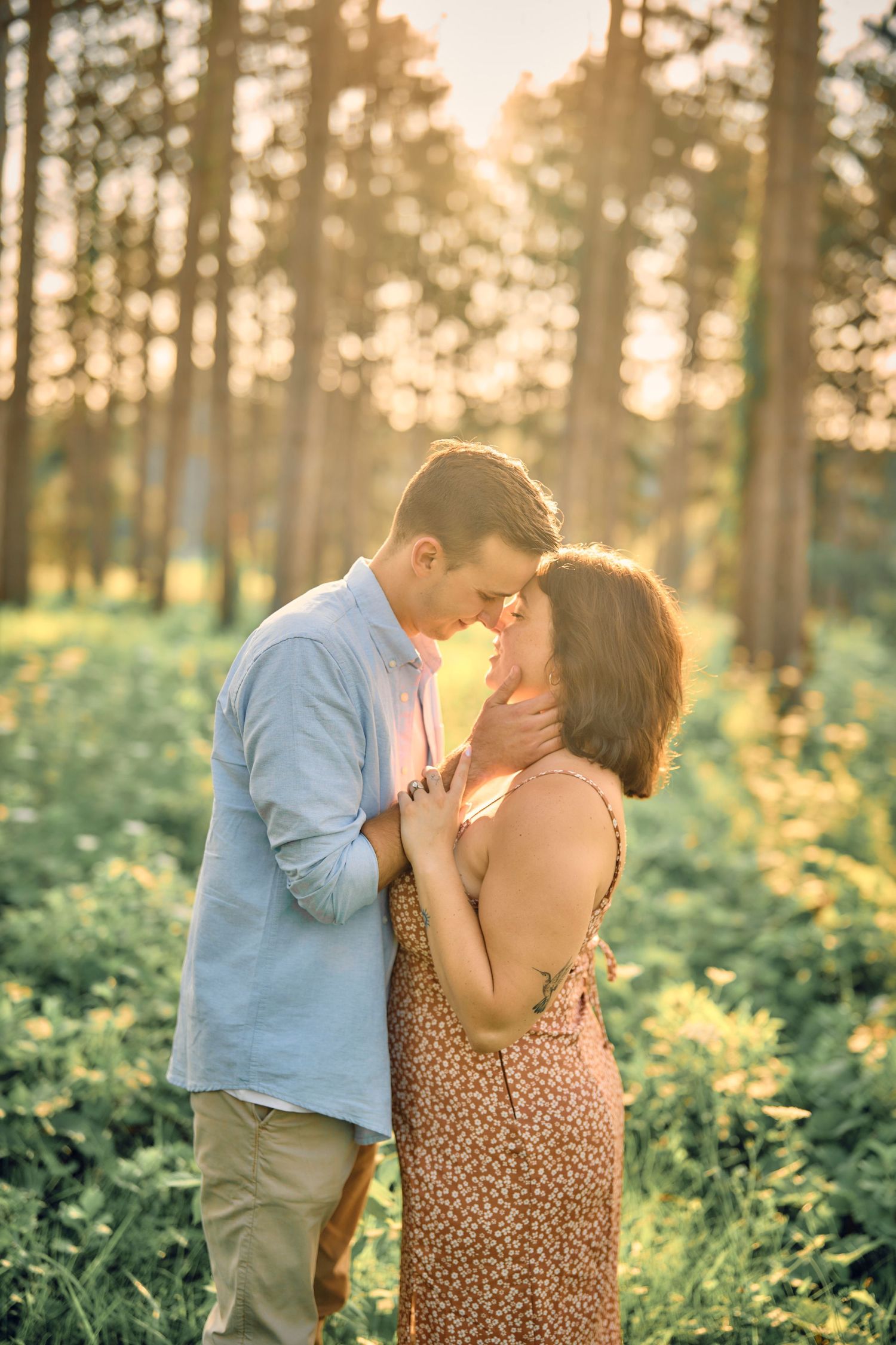 Romantic couple sharing an intimate moment in a sunlit forest with golden light filtering through pine trees.