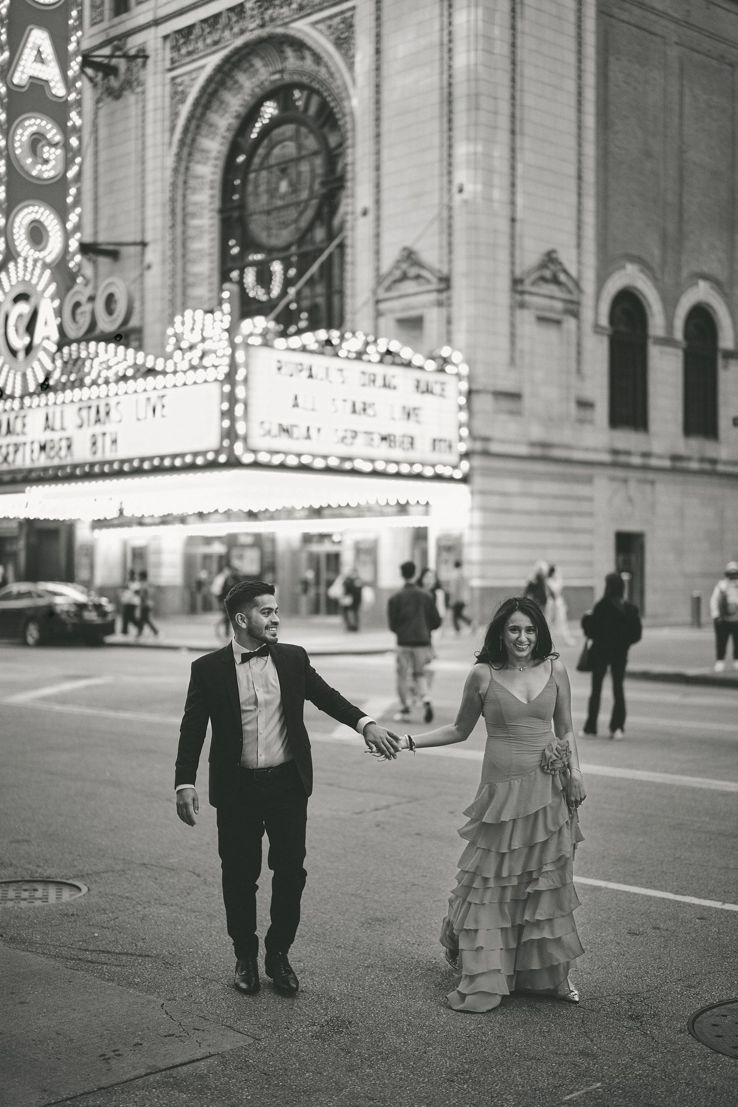 A couple walks hand in hand outside the historic Chicago Theatre with its illuminated marquee in black and white.
