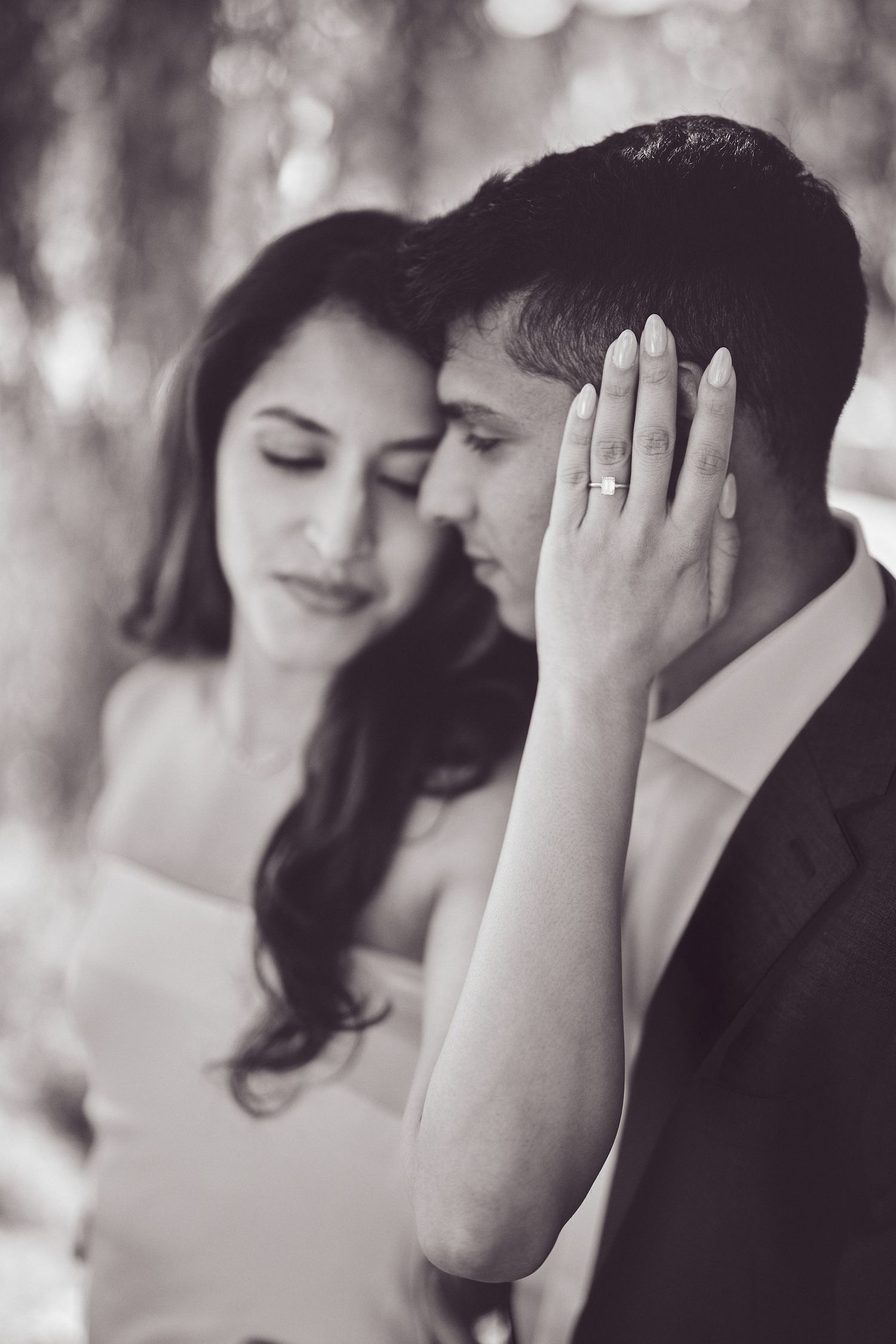 Black and white romantic photo showing a tender intimate moment with hand caressing during what appears to be a wedding shoot.