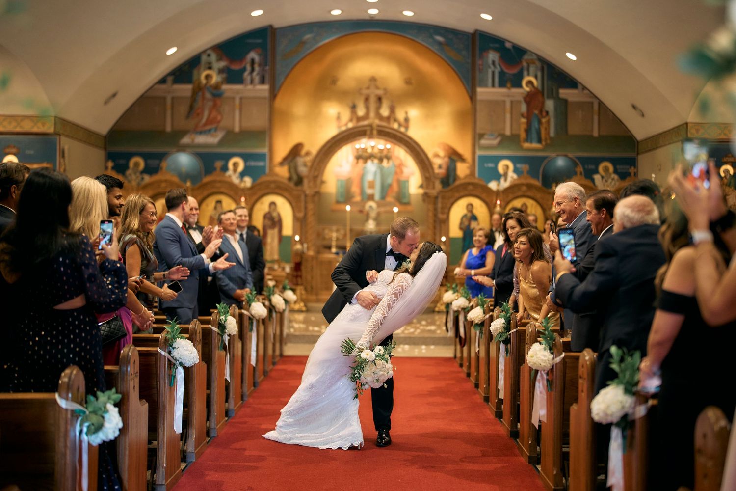 Decorated church interior during wedding ceremony with red carpet aisle and turquoise bows on wooden pews.
