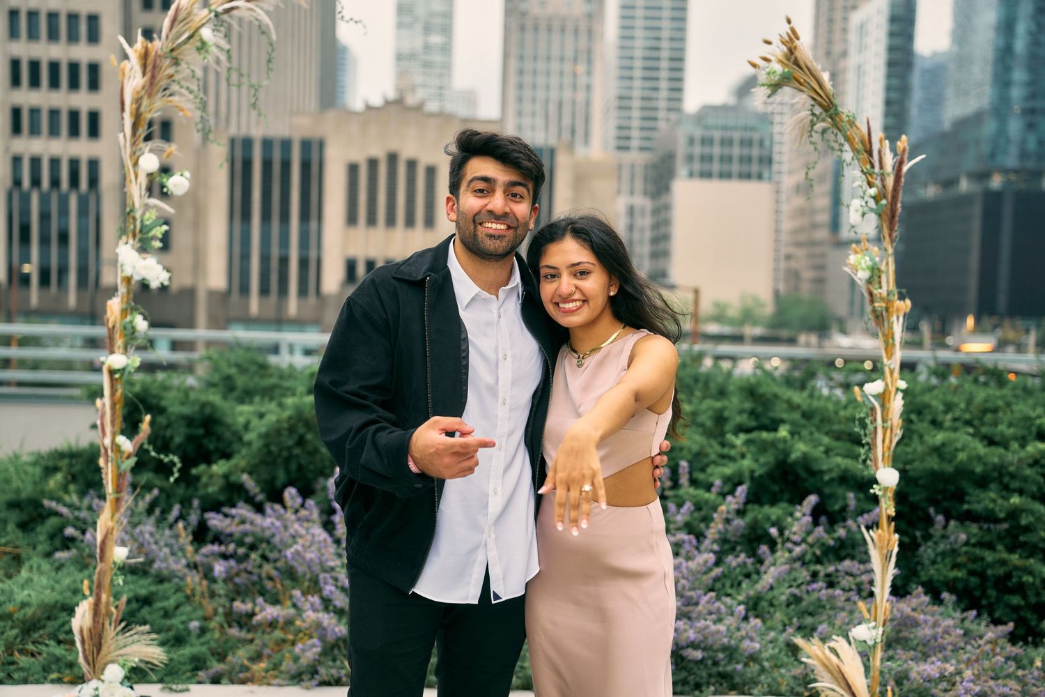 A couple stands together against the Chicago skyline in a garden setting with decorative floral arches.