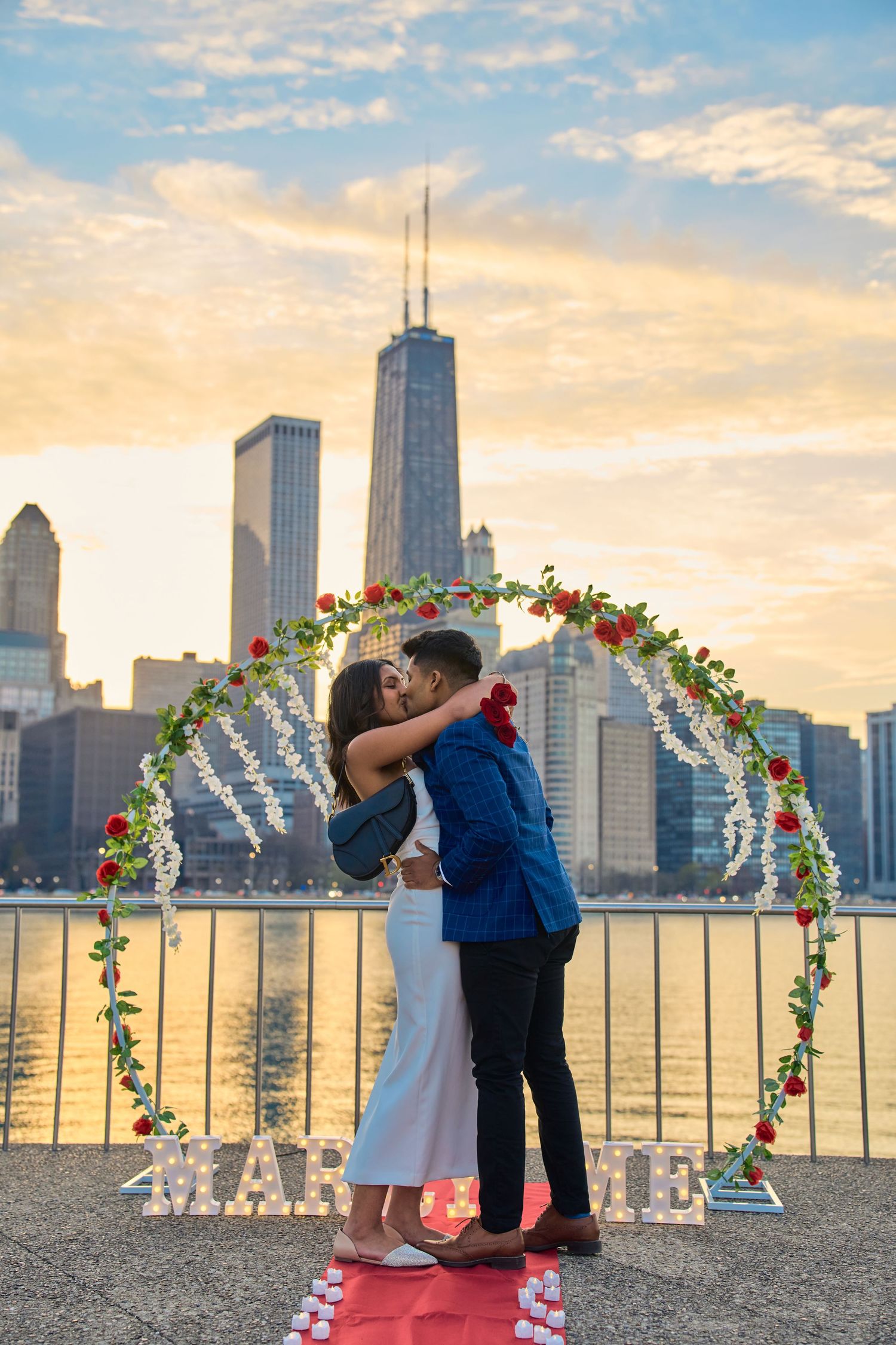 A couple embraces under a floral arch with Chicago's iconic skyline and John Hancock building at sunset over Lake Michigan.