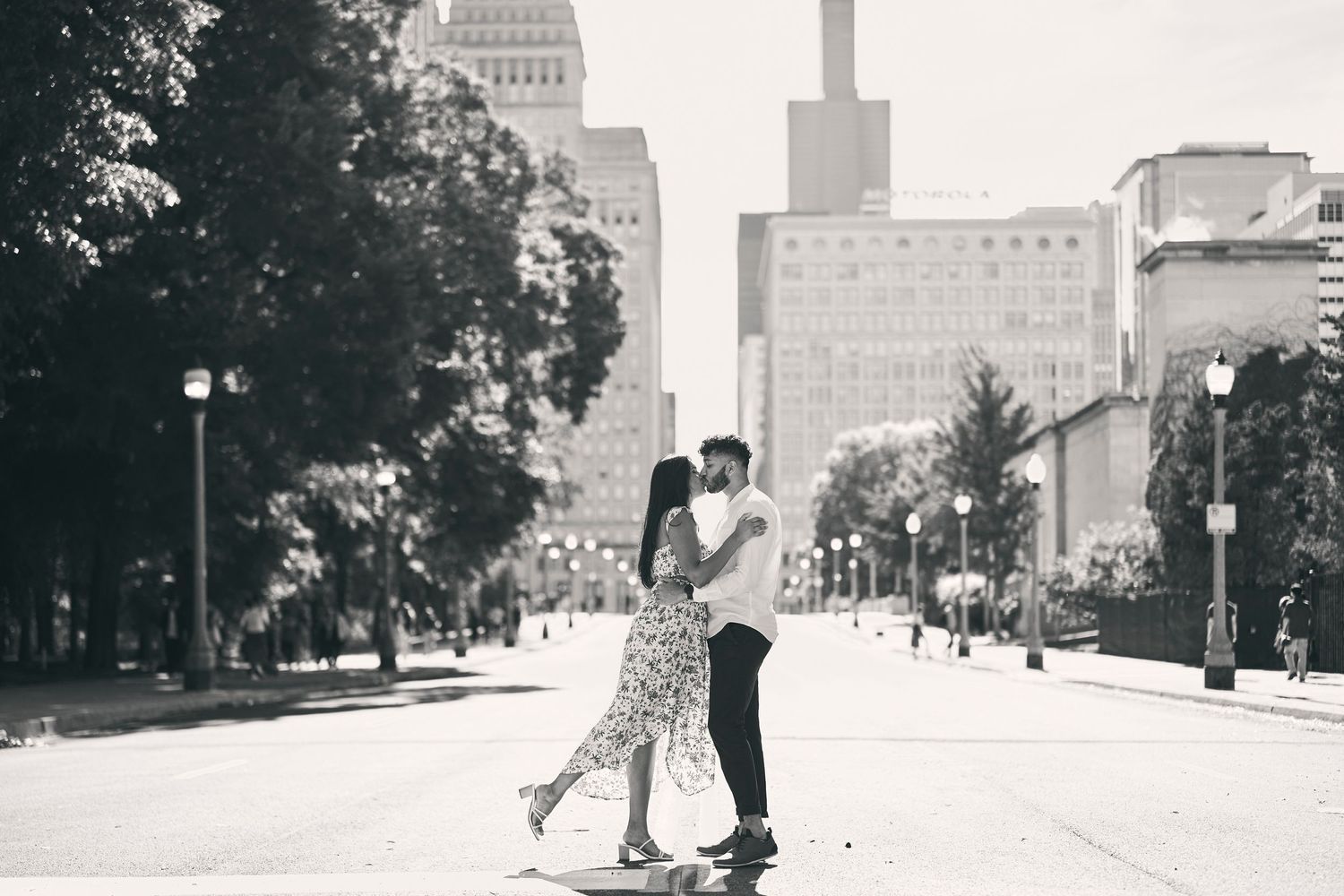 A romantic couple dances together on an empty city street with urban buildings and a cloudy sky in the background.