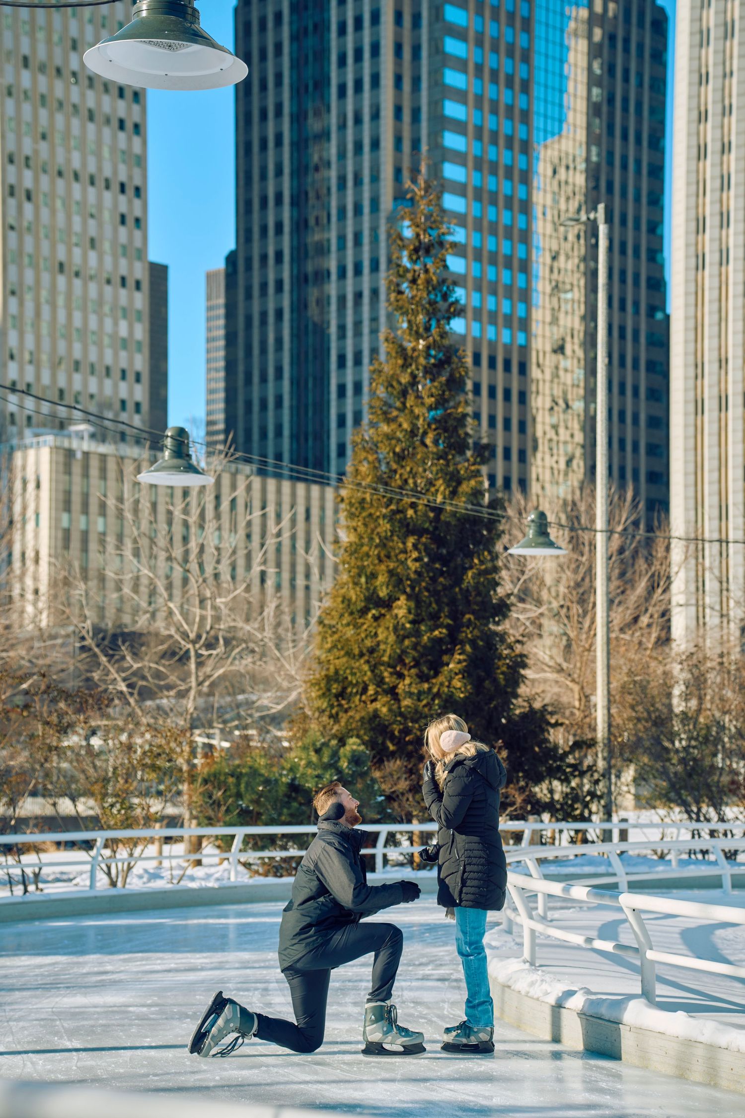 A couple shares a special moment on an ice skating rink with city skyscrapers in the background.