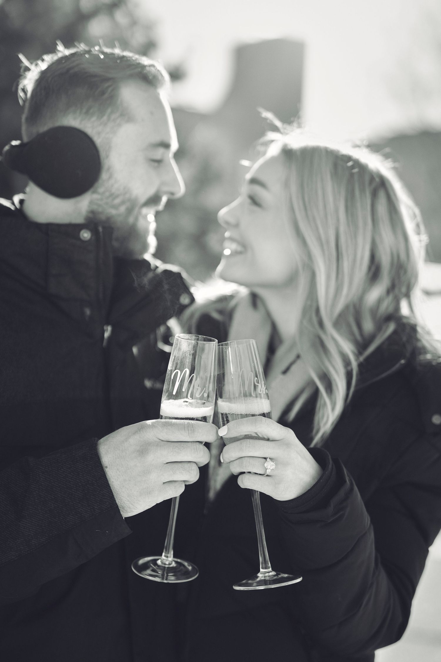 A romantic couple shares champagne glasses while enjoying an intimate black and white moment together outdoors.