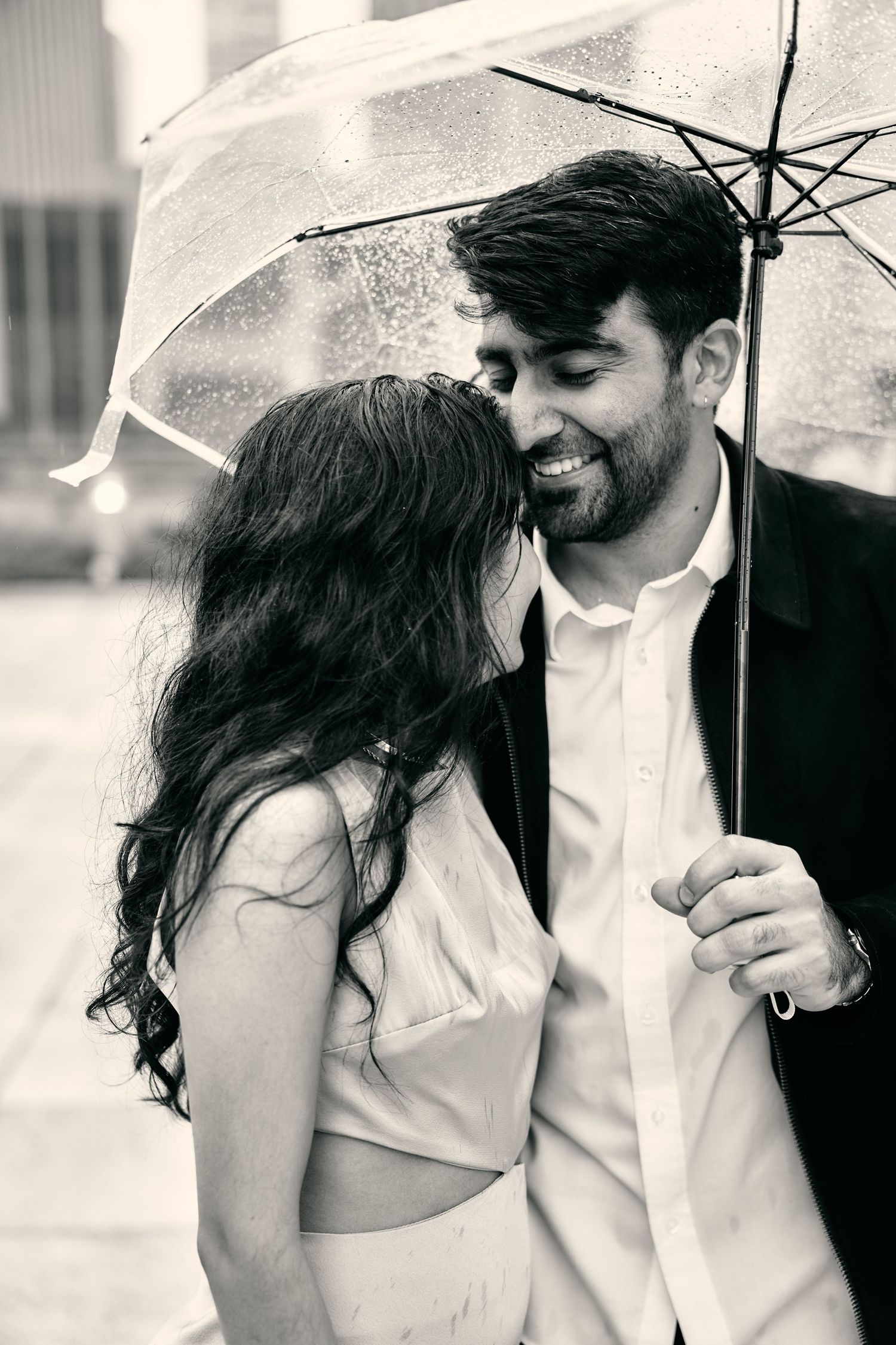 A romantic black and white photo series showing a couple sharing intimate moments under a clear umbrella in the rain.