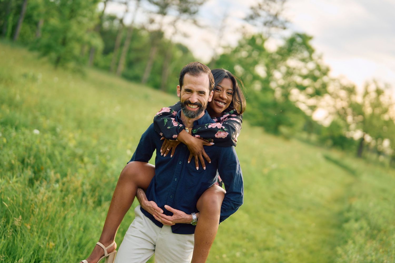 Two people smiling joyfully while piggyback riding in a green summer field at sunset.