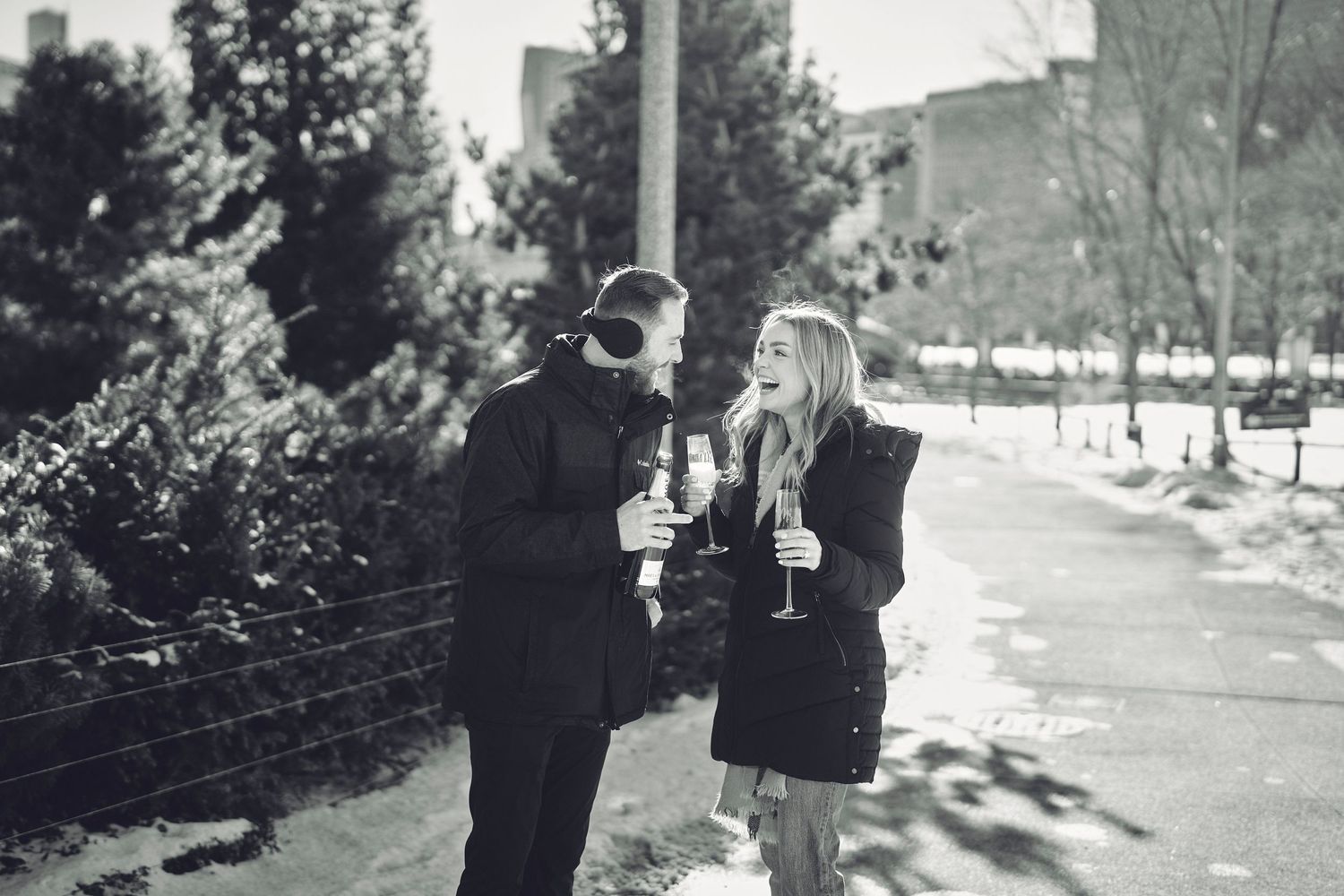 Two people stand together on a snowy winter path sharing drinks in black and white vintage photograph.