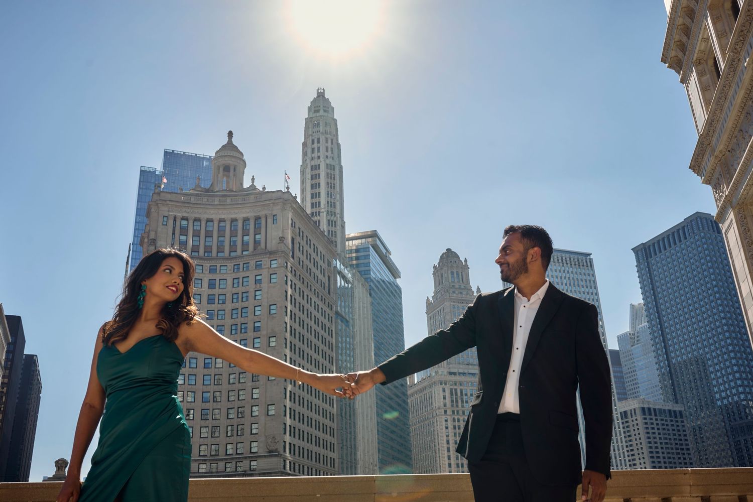 Couple holds hands against Chicago skyline background with historic Wrigley Building and skyscrapers on sunny day.