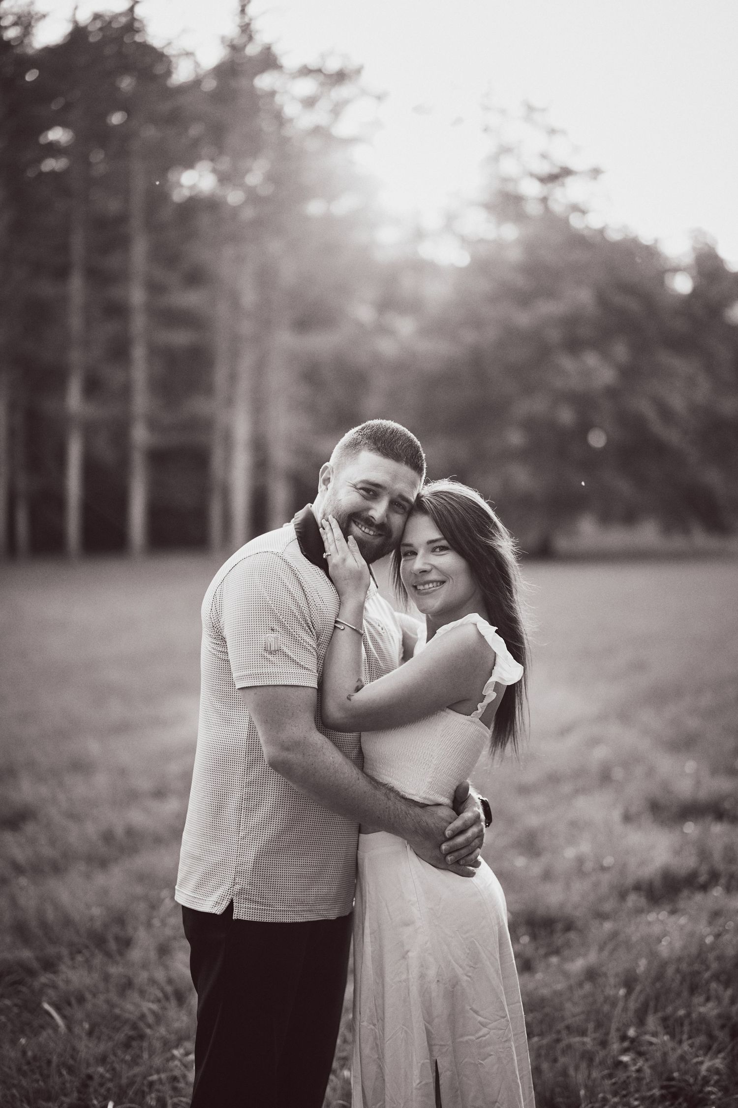 A romantic black and white photo of an embracing couple sharing a tender moment in a misty forest clearing.