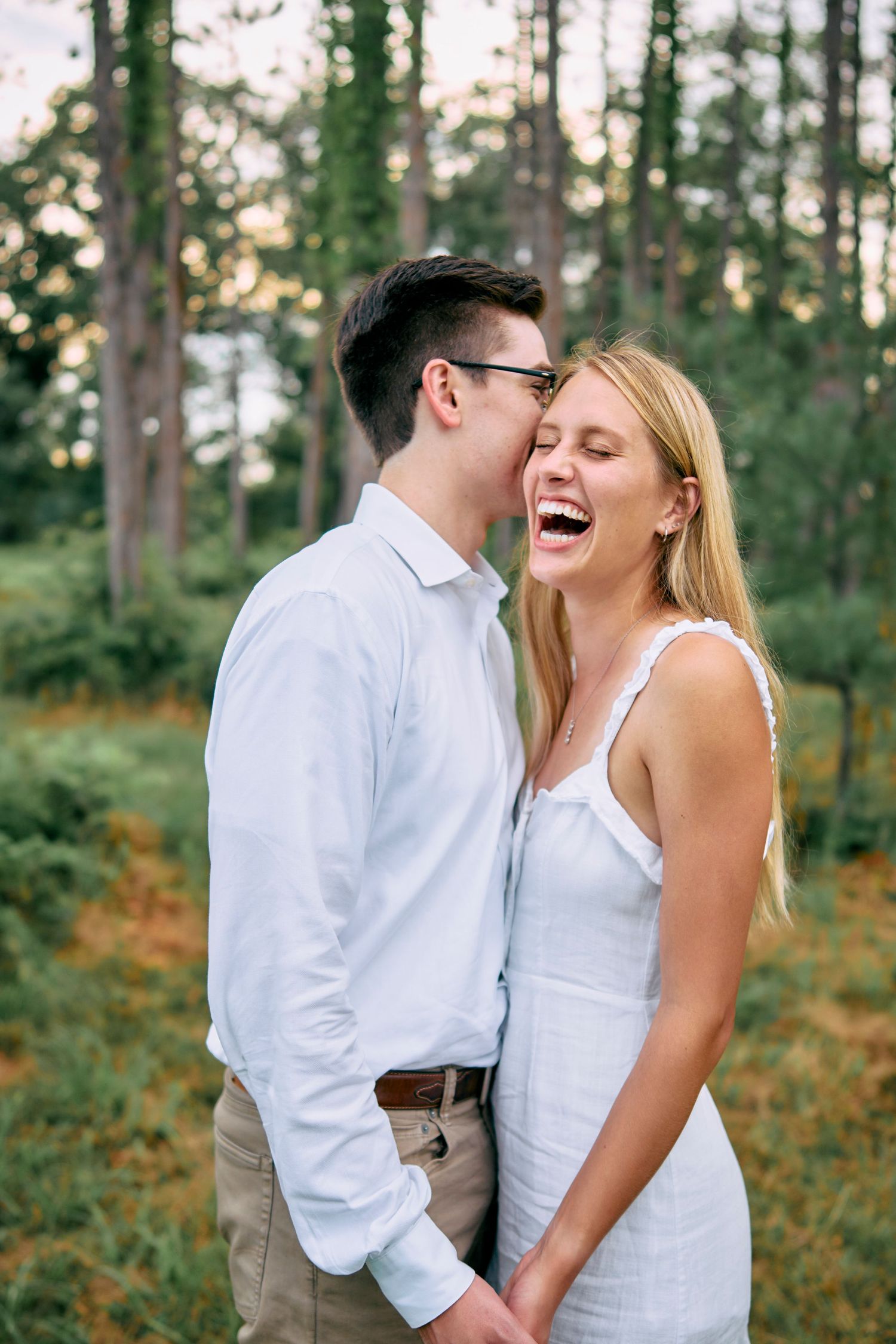 A joyful couple shares a candid moment together laughing in a sunlit forest setting.