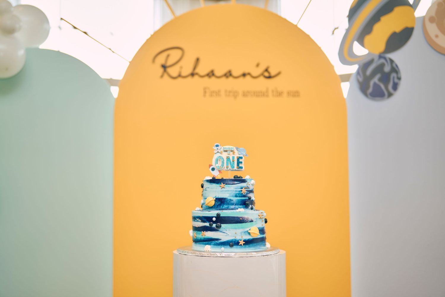 Blue and white tiered celebration cake displayed under yellow arch with name text.