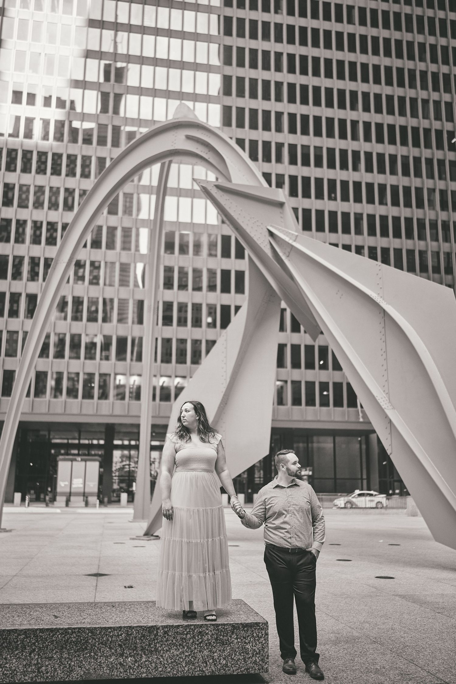 A couple stands beneath the iconic Flamingo sculpture in downtown Chicago, with modern office buildings in the background.
