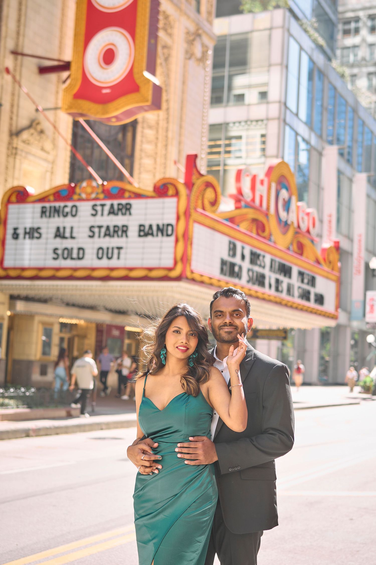 A couple poses together outside a historic theater with a marquee displaying 