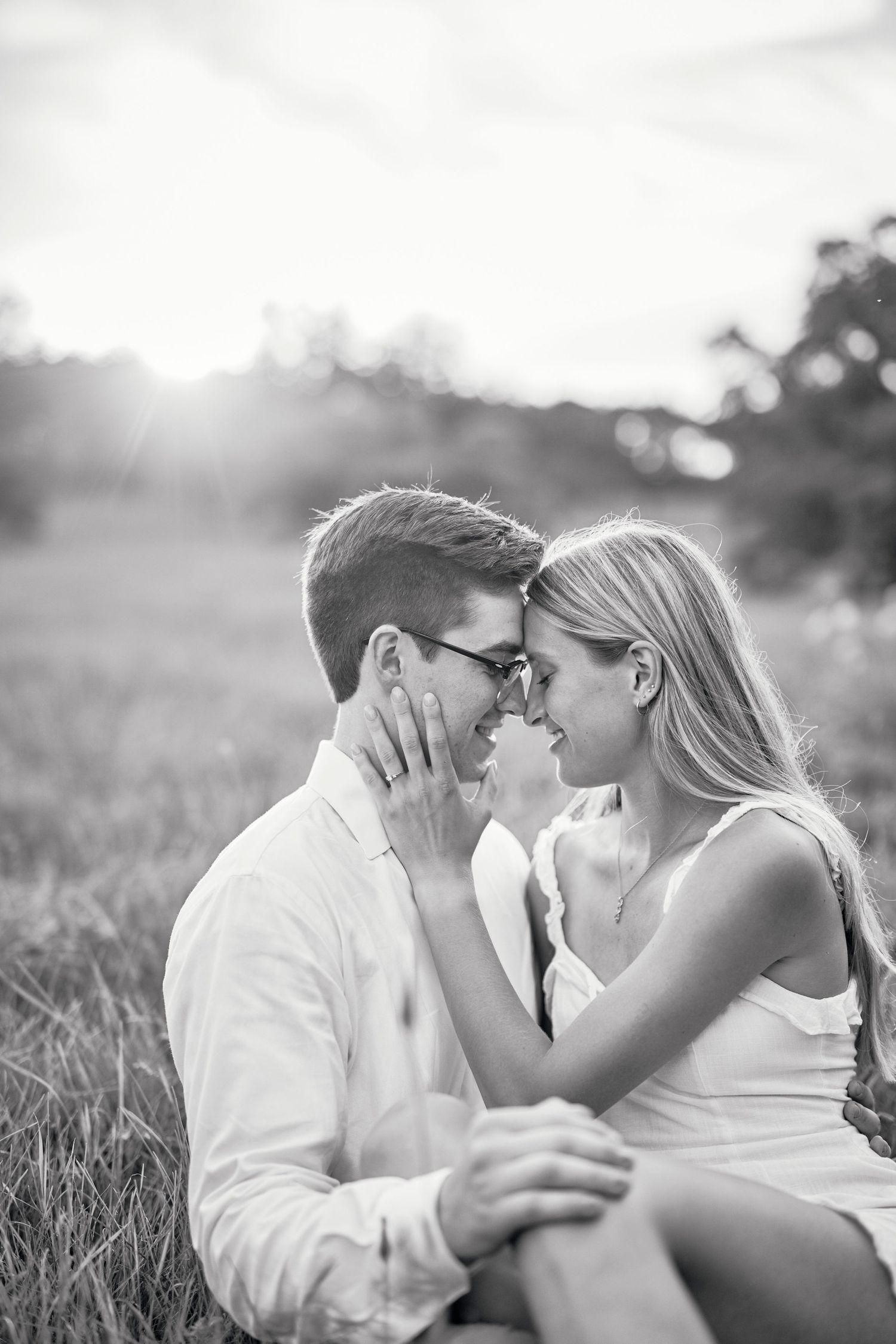 A romantic black and white portrait of a couple sharing an intimate moment in a sunlit meadow.