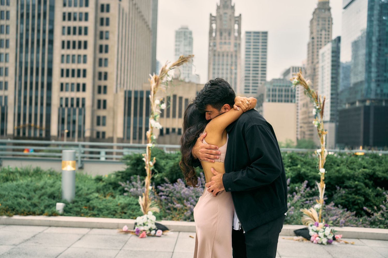 A romantic embrace on a rooftop terrace overlooking Chicago's iconic downtown skyline during sunset.