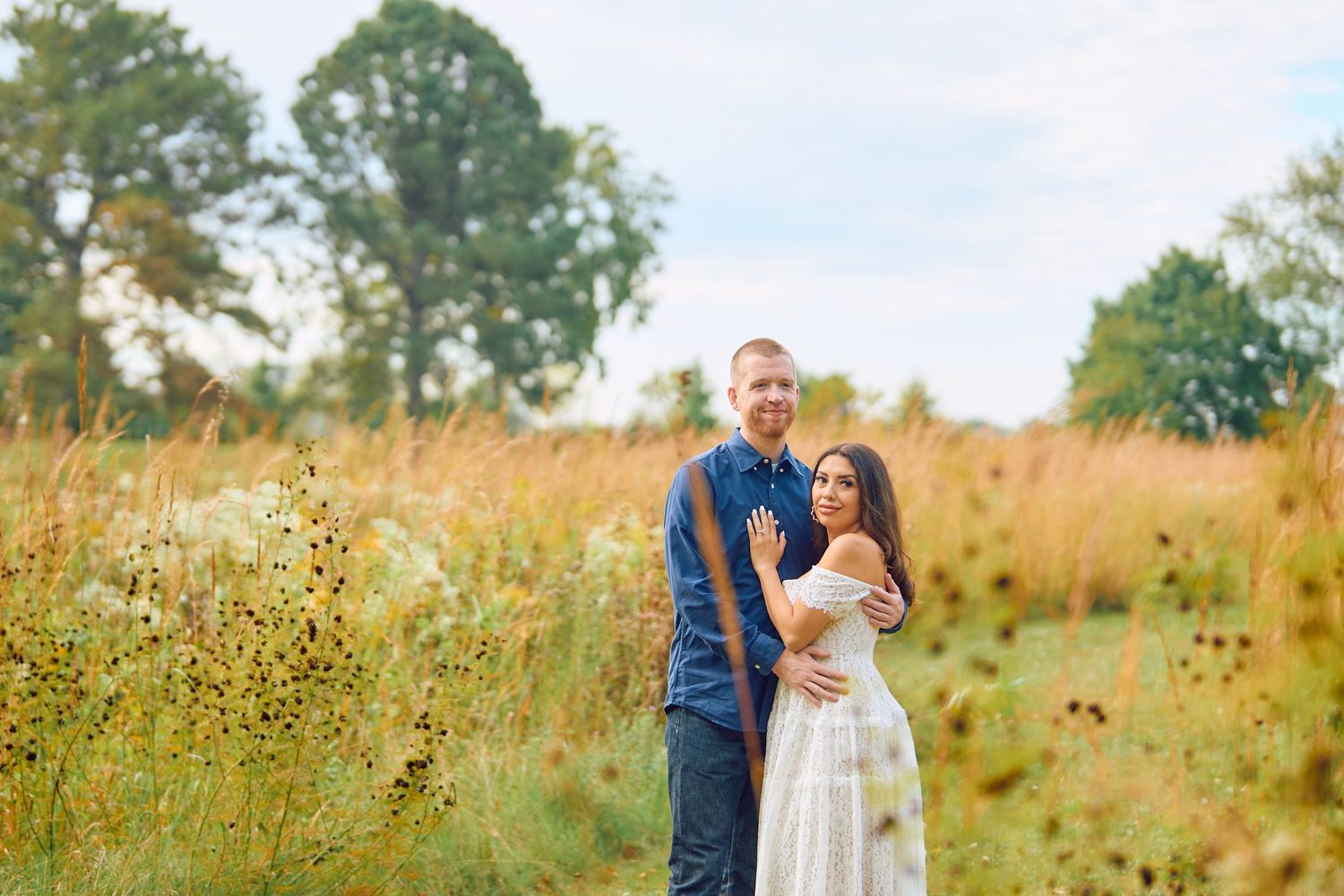 A couple embraces in a golden meadow filled with late summer wildflowers and tall grass at sunset.