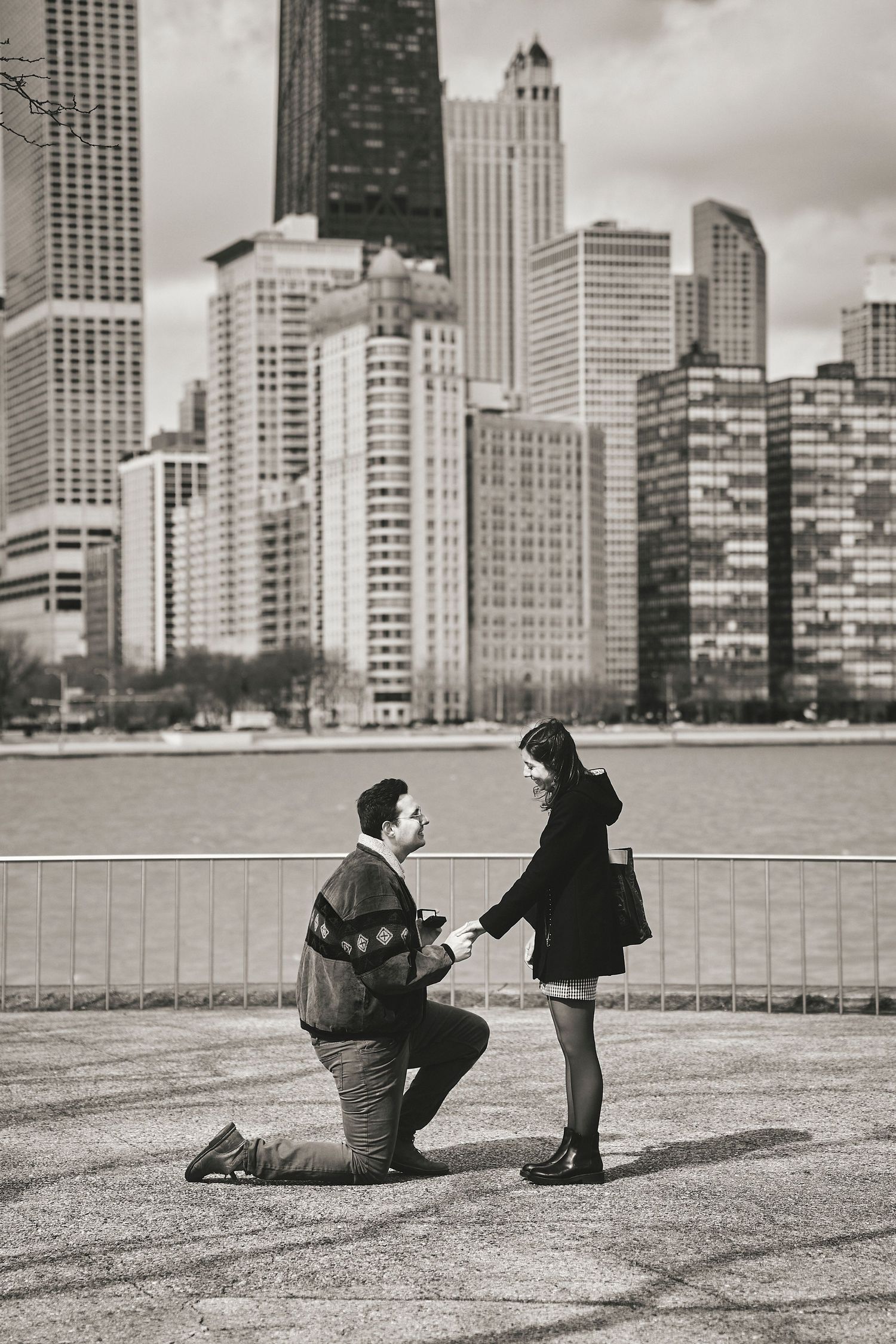 A romantic proposal moment against Chicago's dramatic skyline along Lake Michigan in black and white.