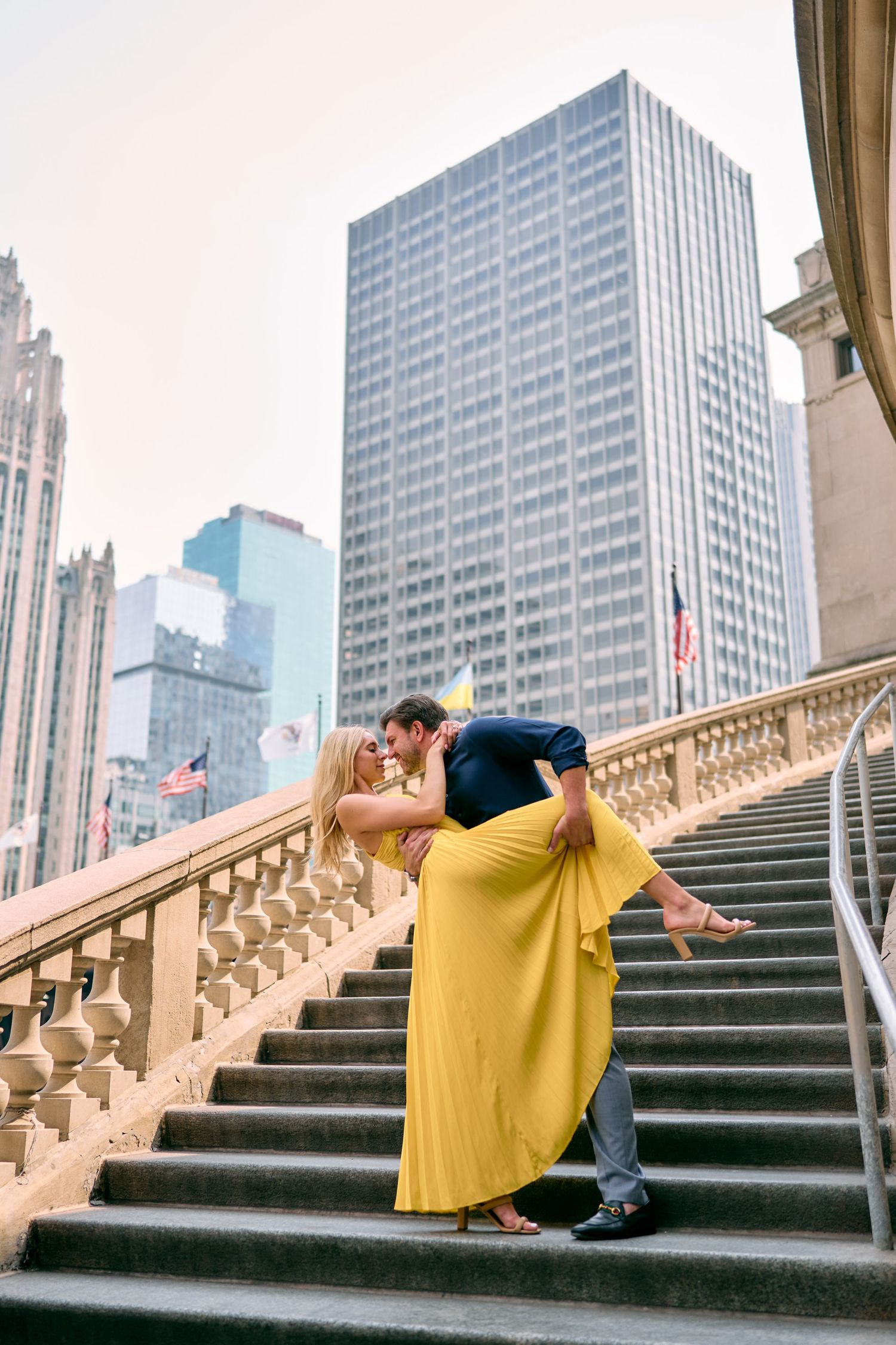 A couple in a romantic pose on stone steps with a yellow dress and urban skyscrapers in the background in Chicago.