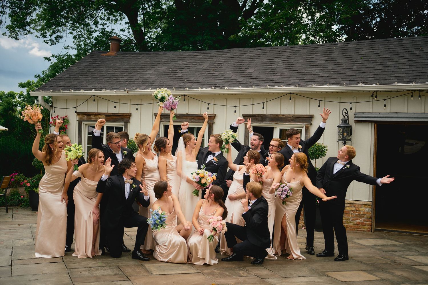 A wedding party celebrates joyfully on an outdoor patio while raising their arms in excitement.