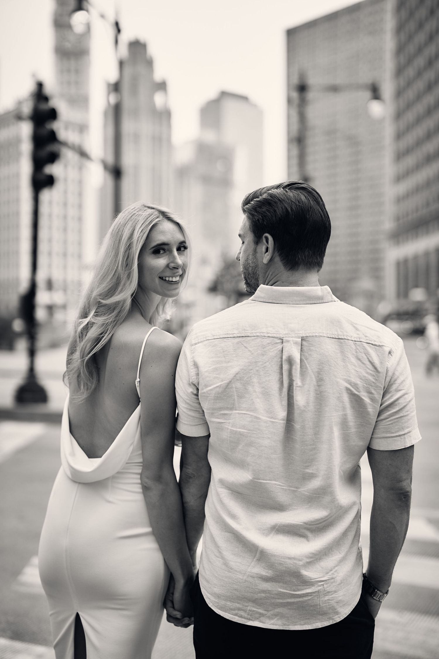A romantic black and white photo of a couple walking together with a city skyline backdrop.