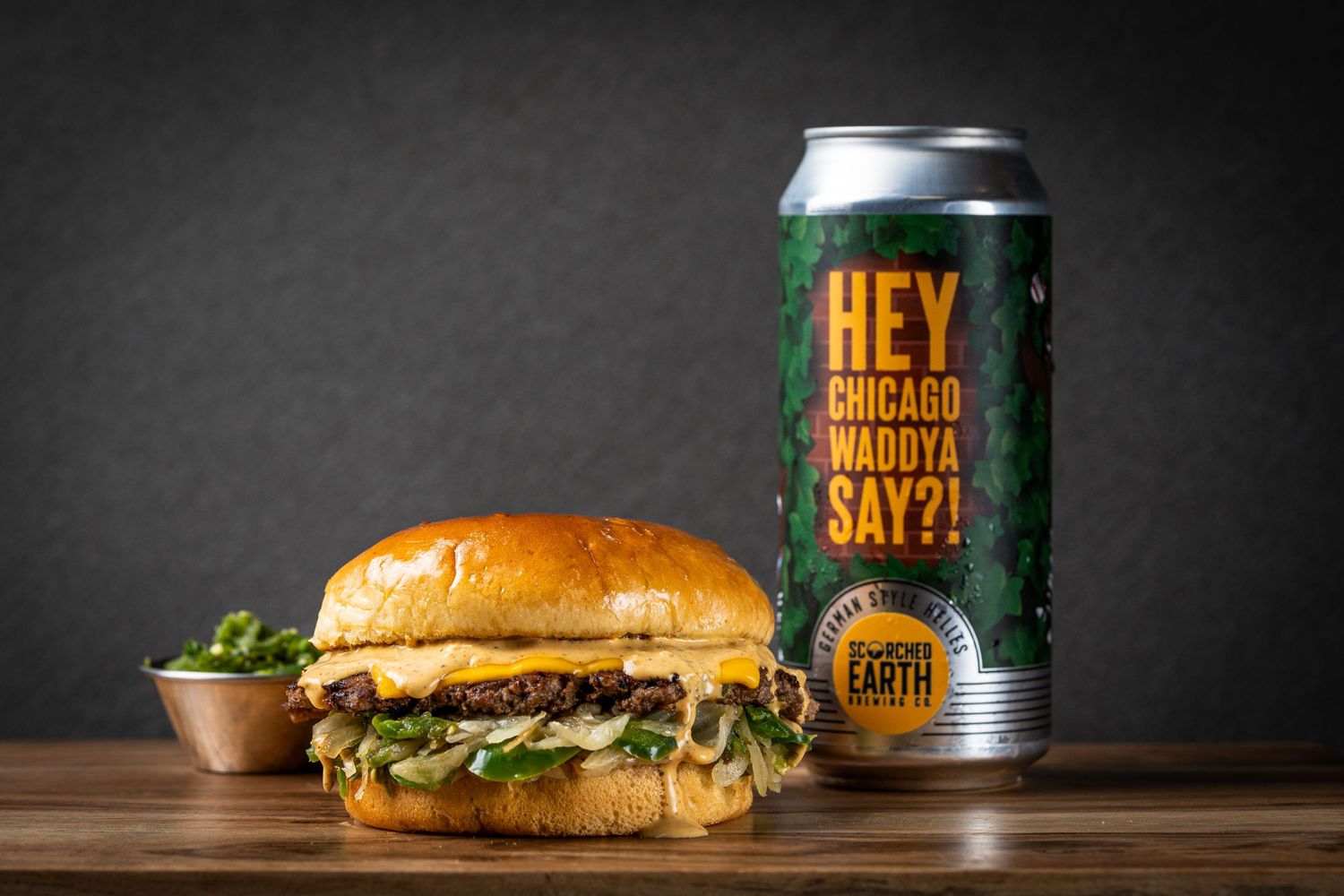 Juicy cheeseburger next to green beer can with 'Hey Chicago' text on dark background.