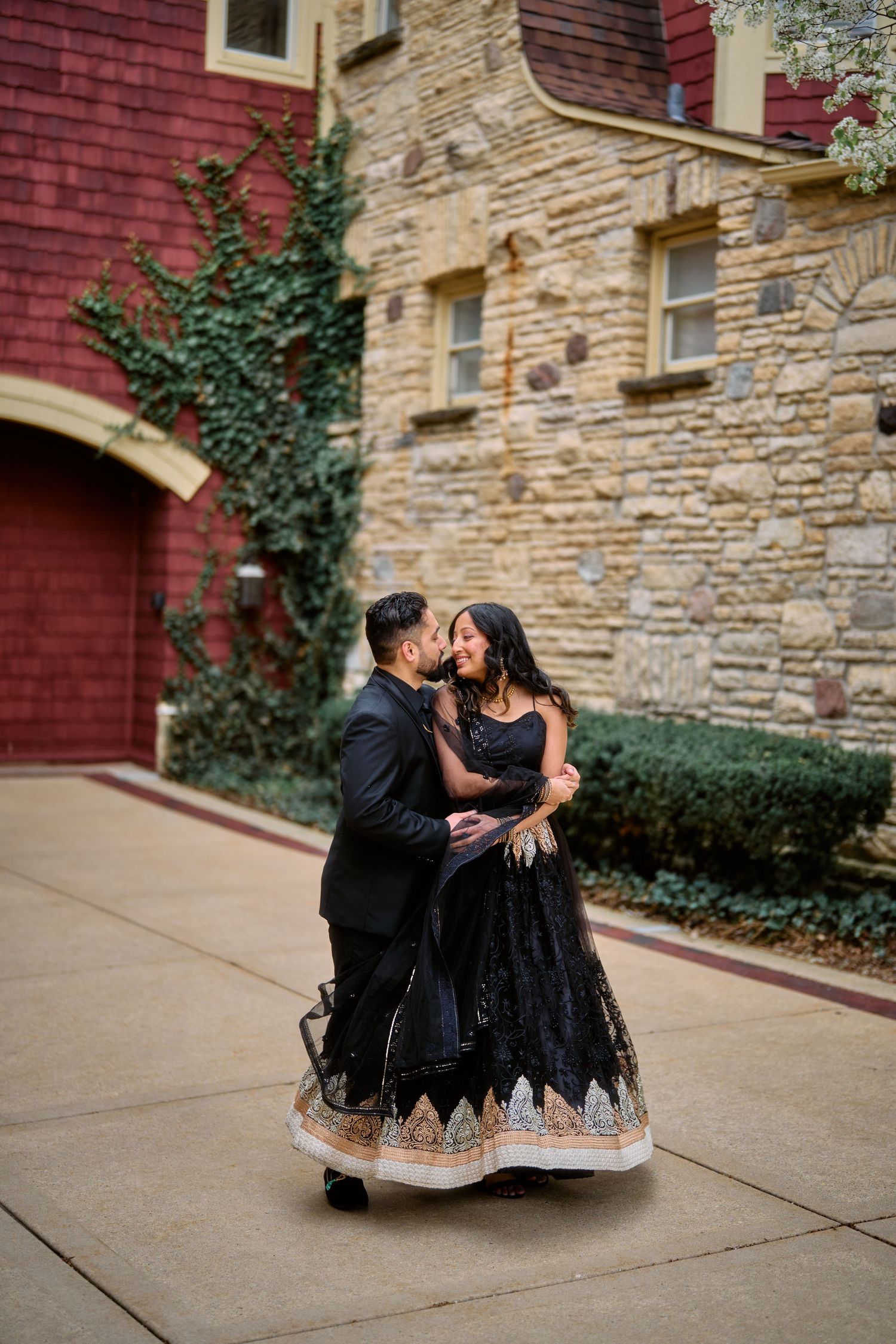 A couple wearing elegant black attire dance together on a sidewalk in front of a stone and brick building exterior.